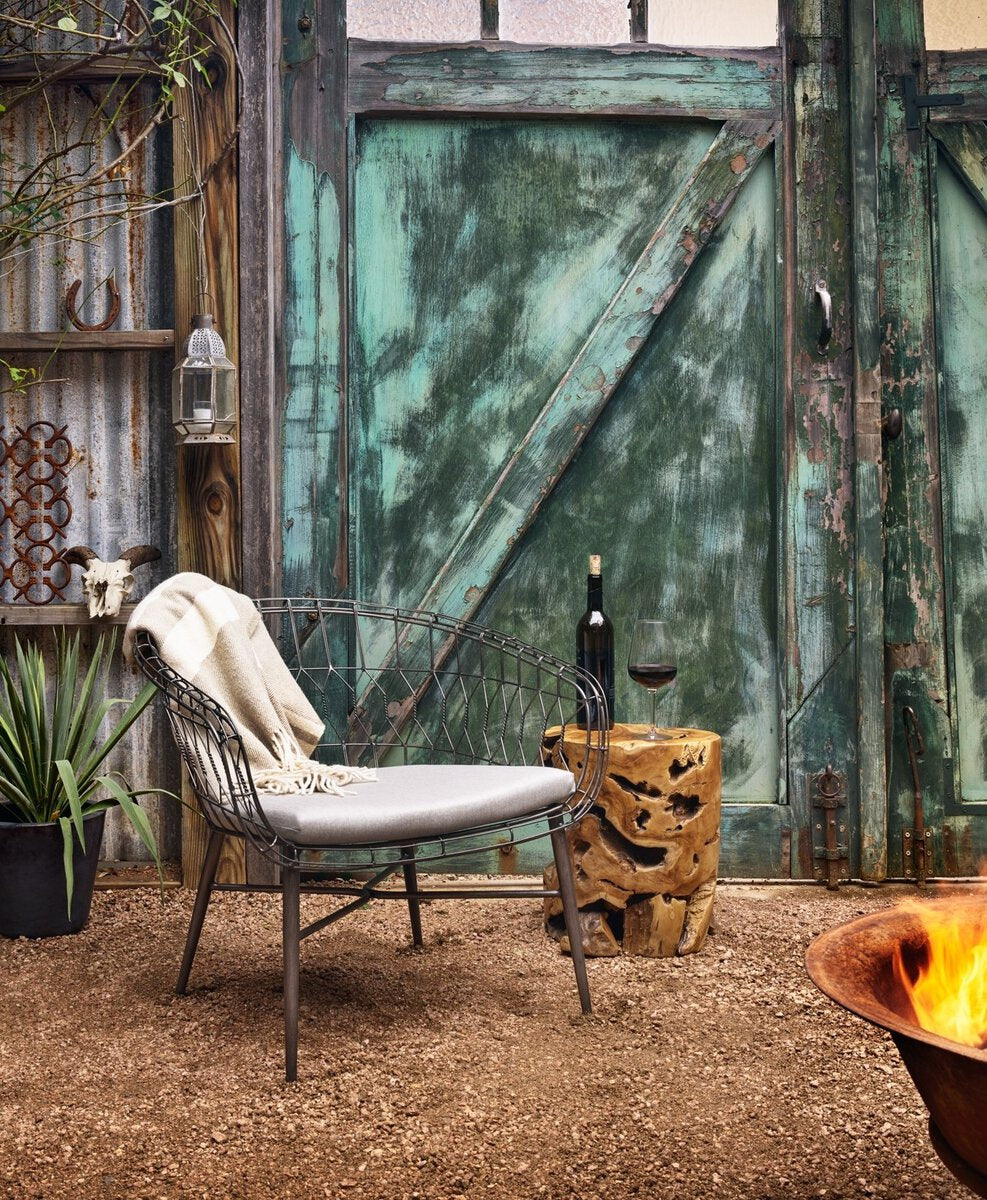 Outdoor setting with a chair, bottle, and glass against a rustic metal gate.