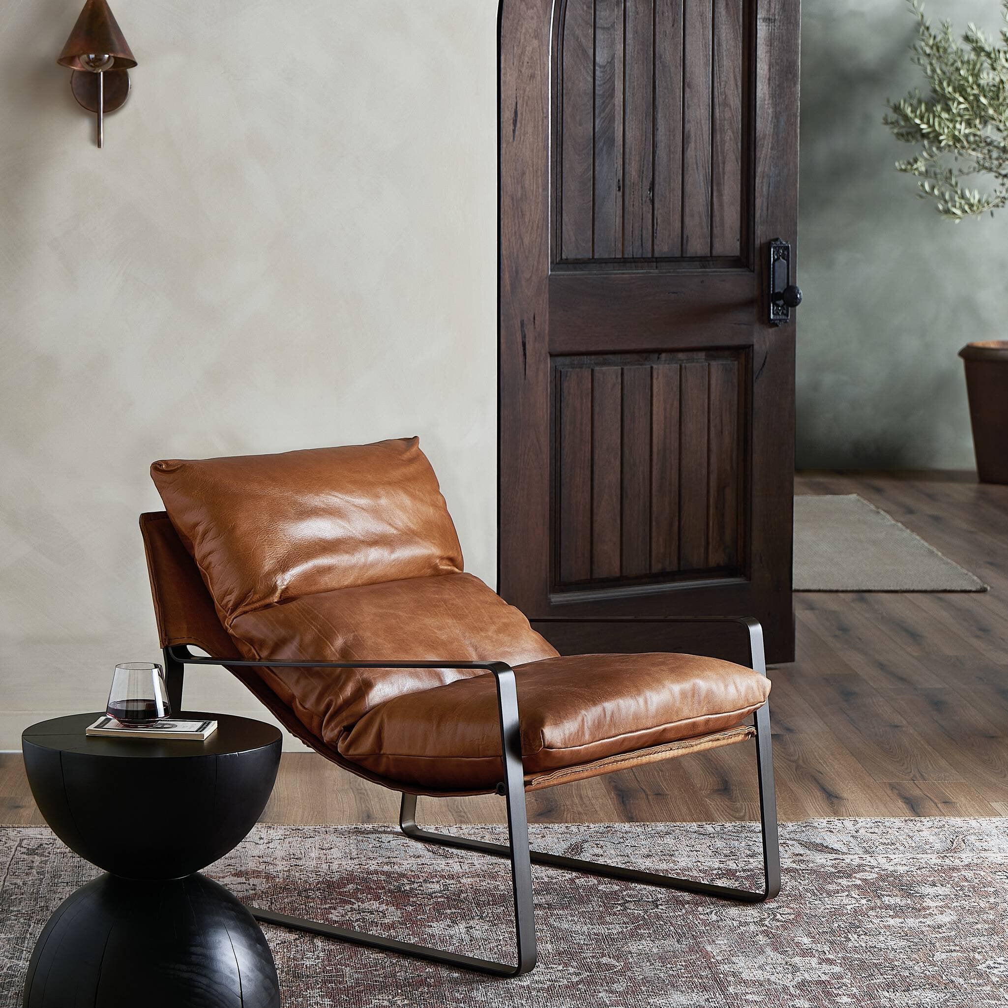 Brown leather lounge chair in a room with wooden door and rug