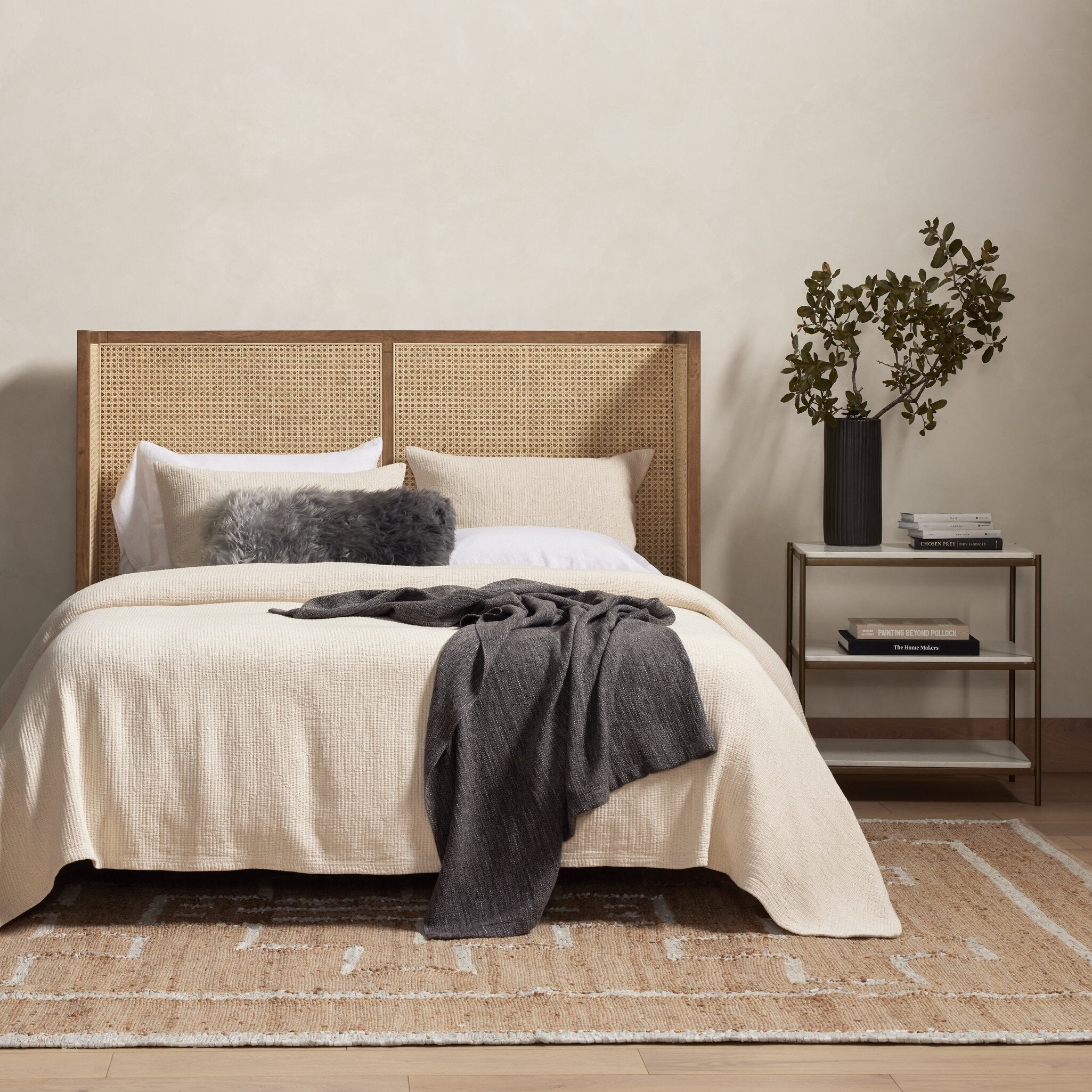 Bedroom with a bed featuring a wicker headboard, beige bedding, and a nightstand with a plant.