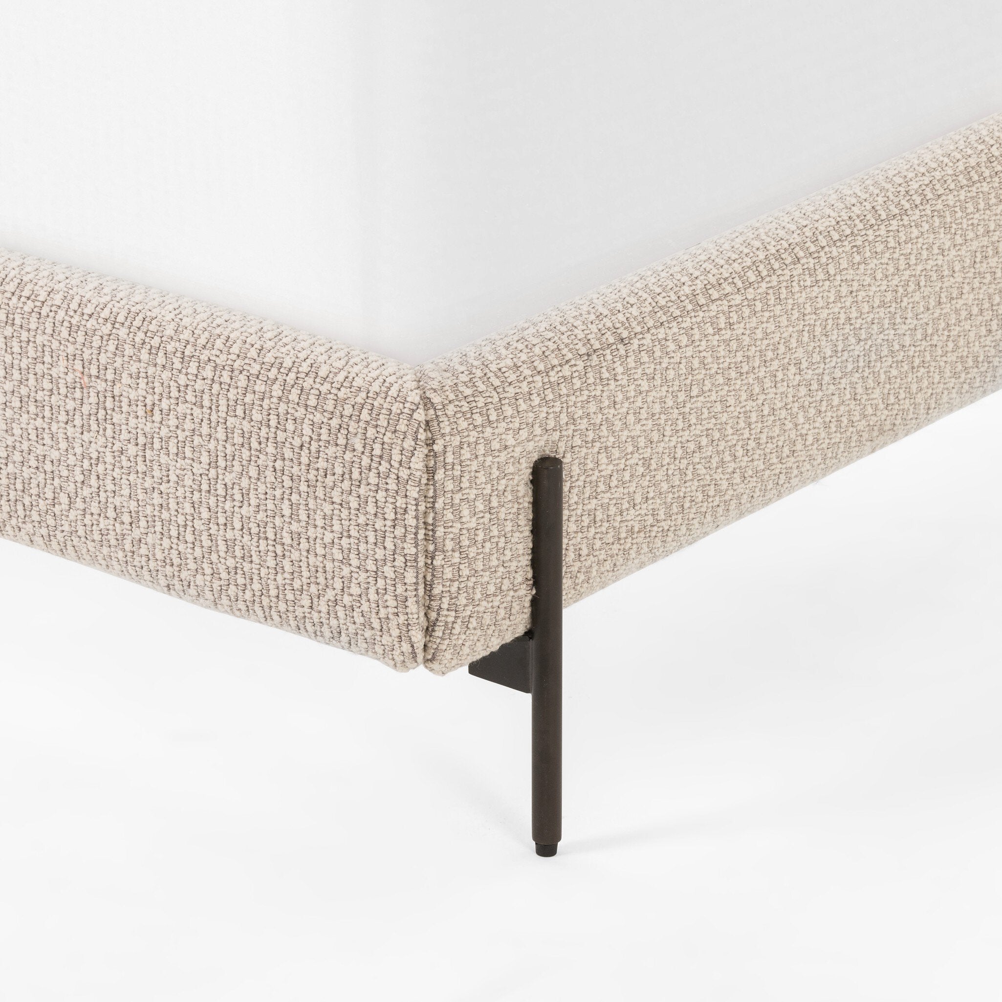 Beige upholstered bed with black metal legs on a white background