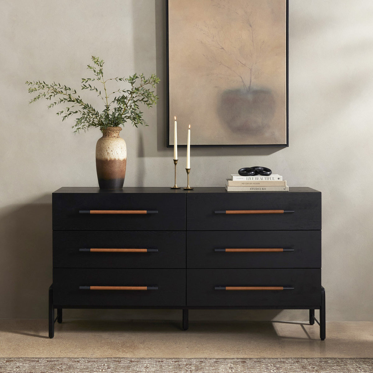 Black dresser with wooden handles in a room setting with a vase and candles on top.