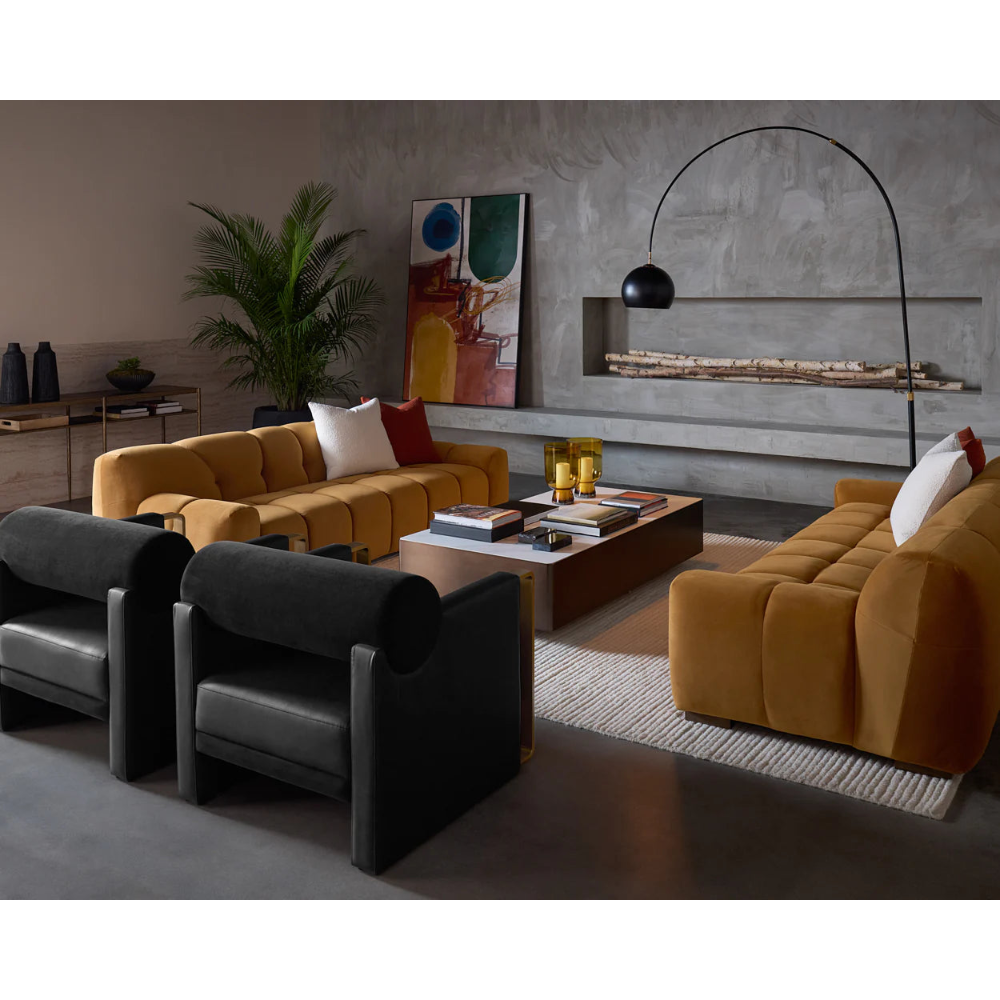 Modern living room with gold sofa, black armchairs, and abstract art on the wall.