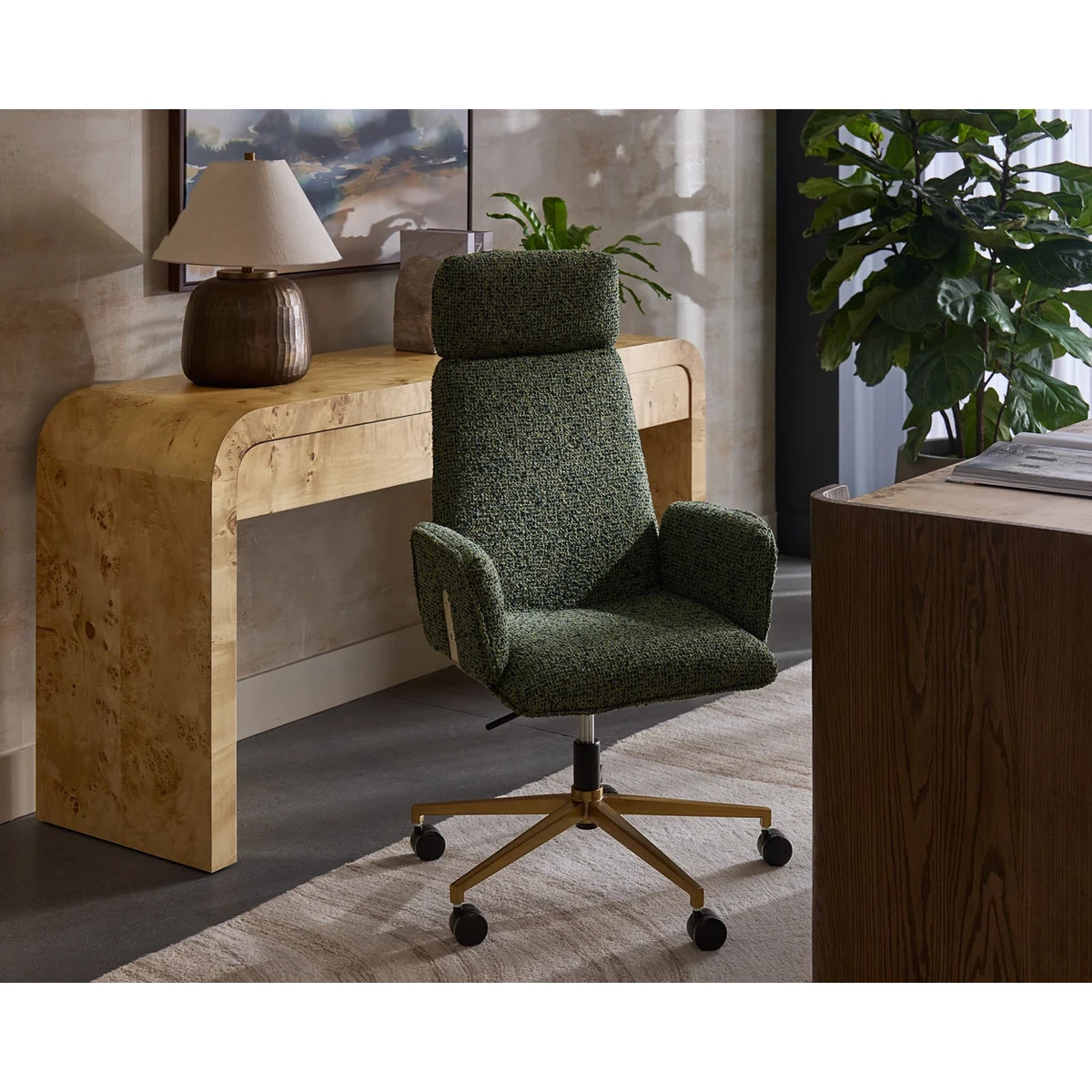 A green textured fabric office chair with a gold five-star base and black casters, positioned in a modern home office setting next to a light wood console table and a potted plant.