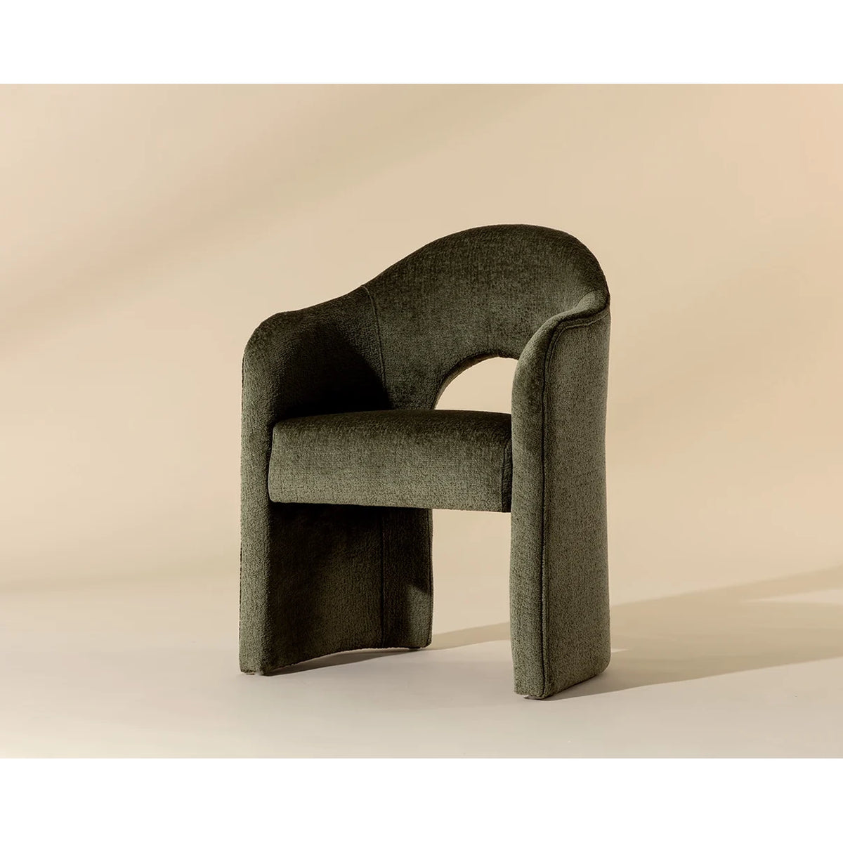 A modern upholstered accent chair in a textured dark olive green fabric, featuring a curved backrest and integrated side tables on each leg, set against a warm beige studio background.