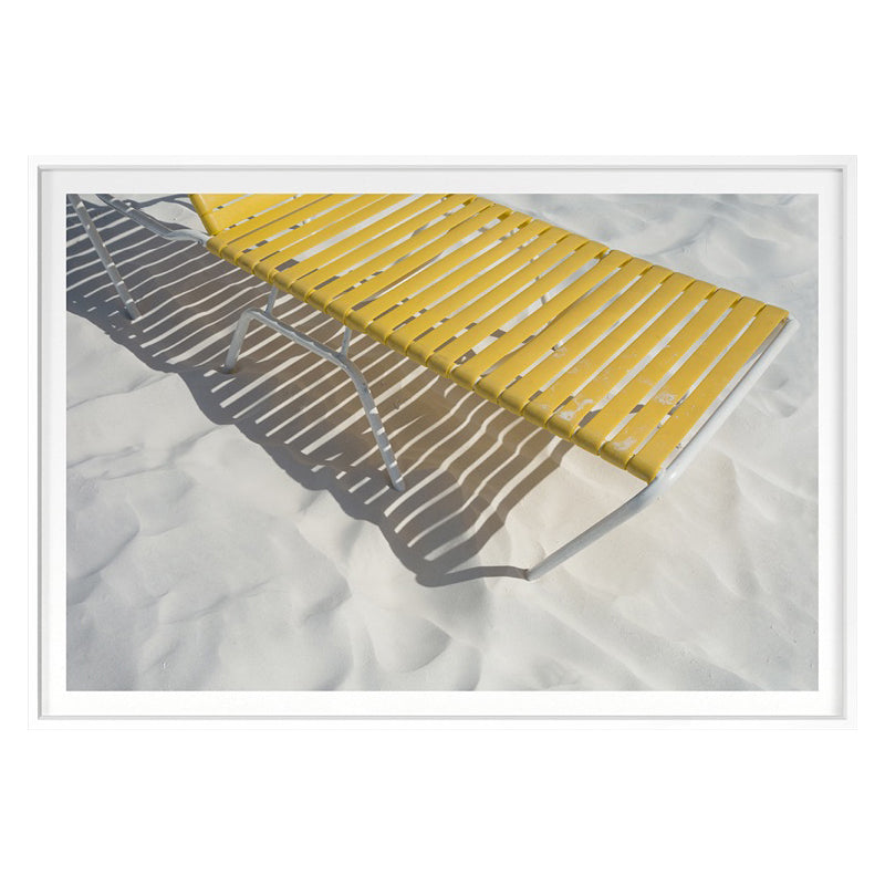 Framed art print of yellow and silver beach chair on sand in white frame
