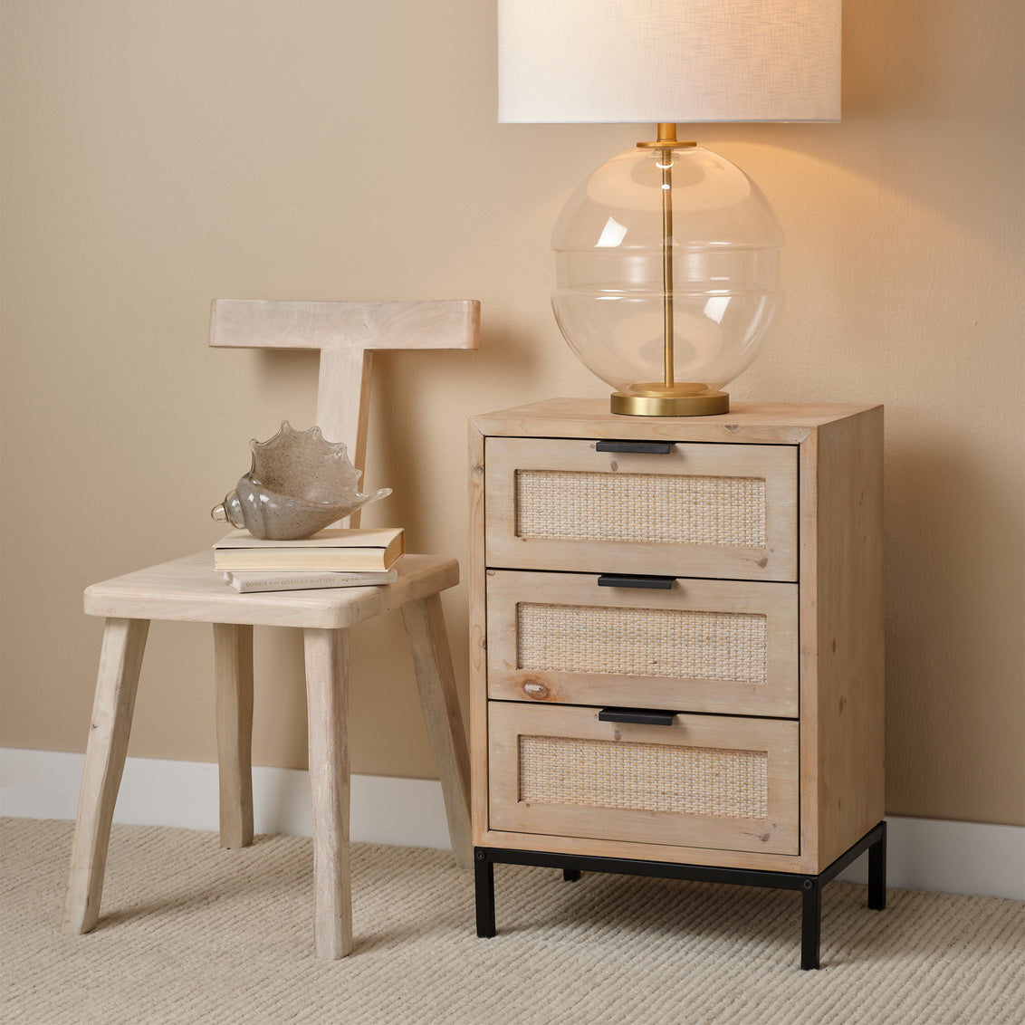 Wooden side table with lamp and decorative items against a beige wall.