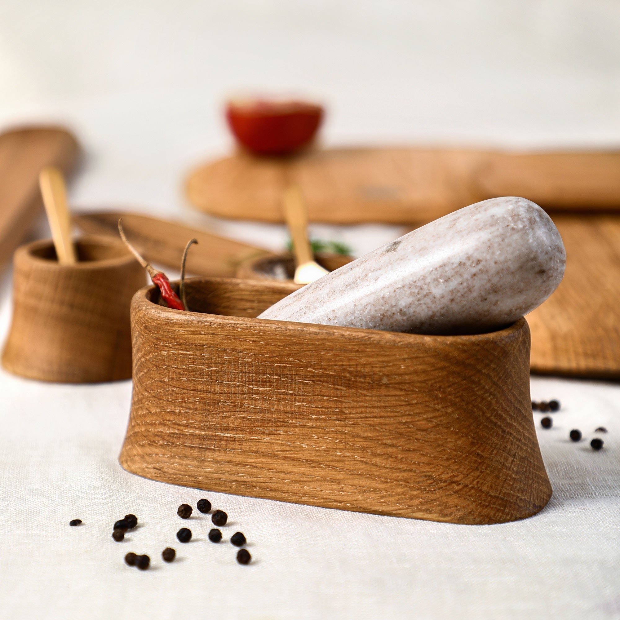 Oak mortar with a stone pestle, surrounded by peppercorns on a light surface.