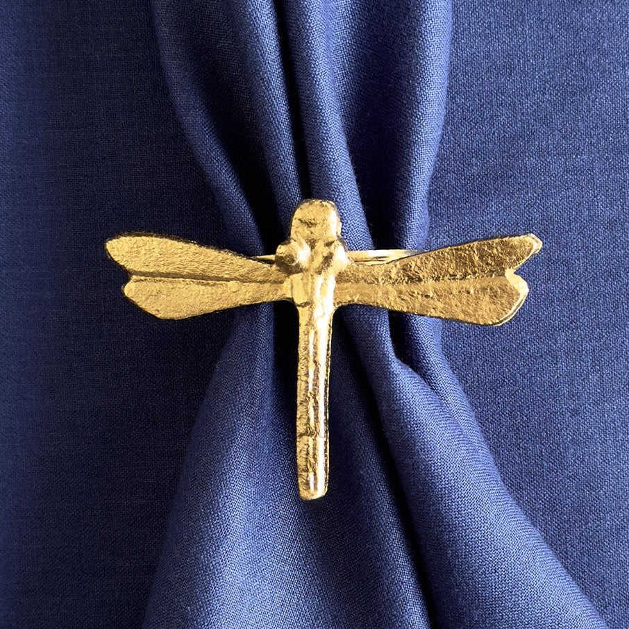 Gold dragonfly-shaped napkin ring on a blue fabric background