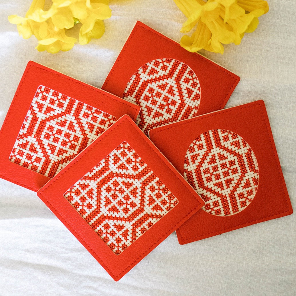 Red coasters with white geometric patterns on a white surface with yellow flowers.