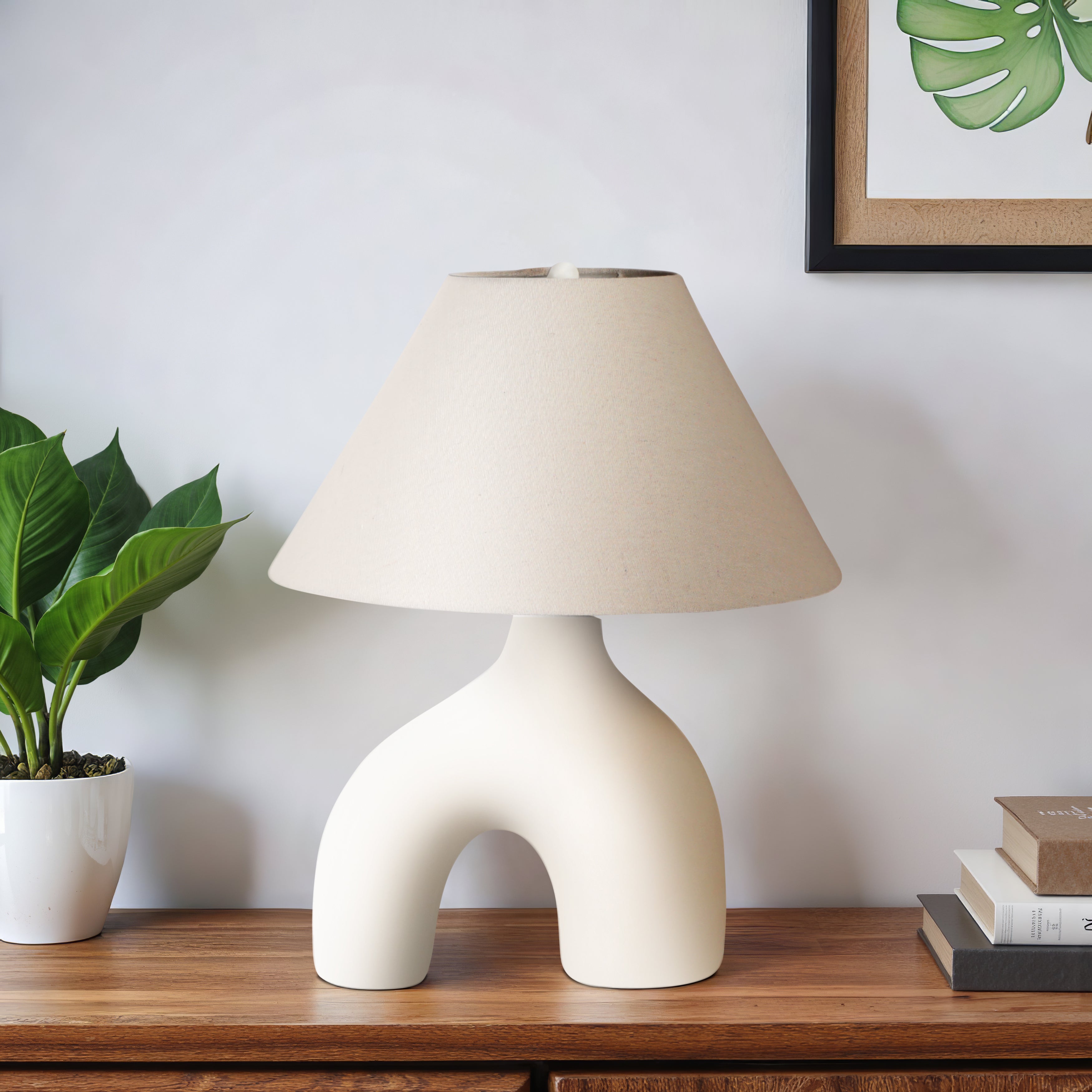 Modern table lamp with a unique base on a wooden surface next to a plant and books.