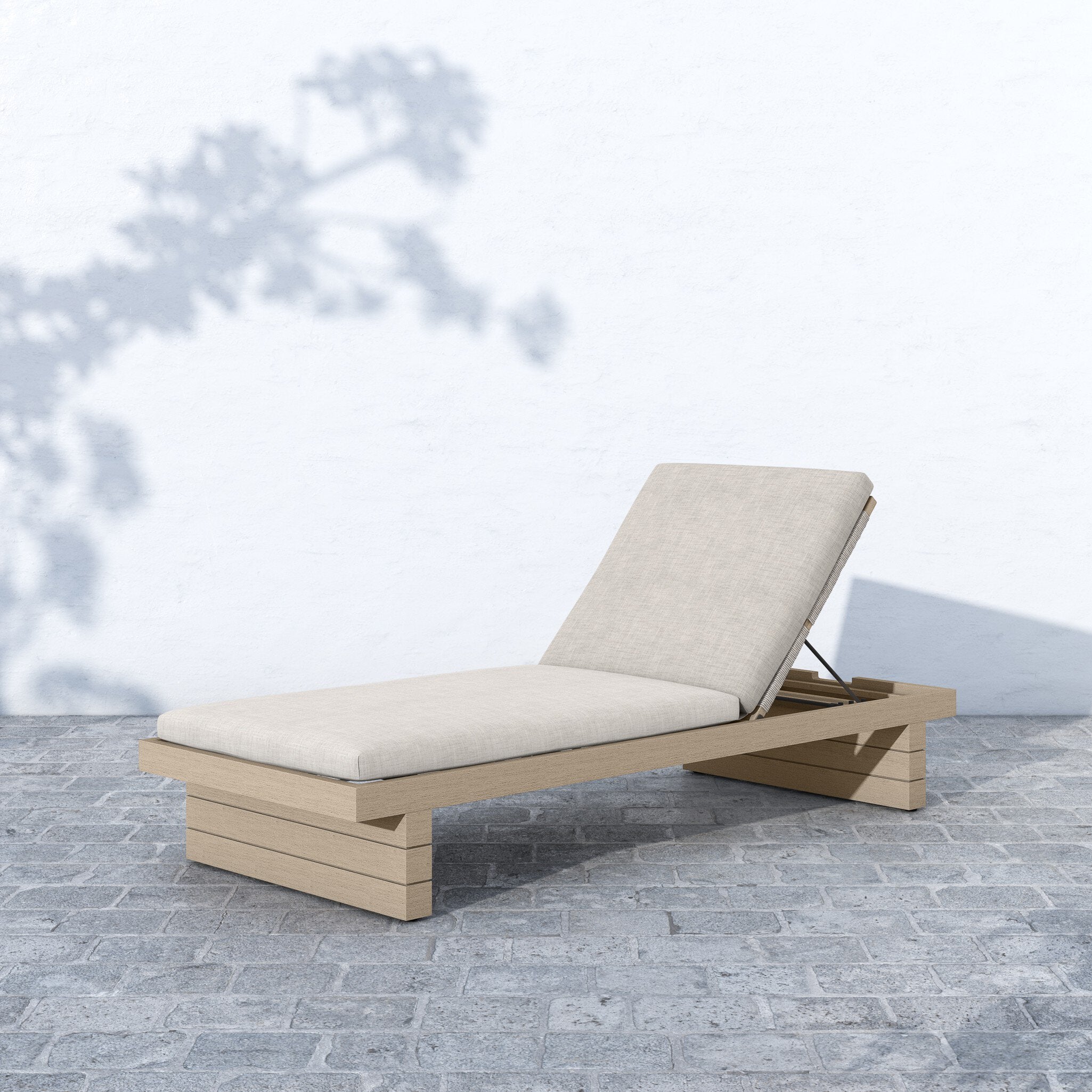 Beige outdoor lounge chair with cushion on a stone patio