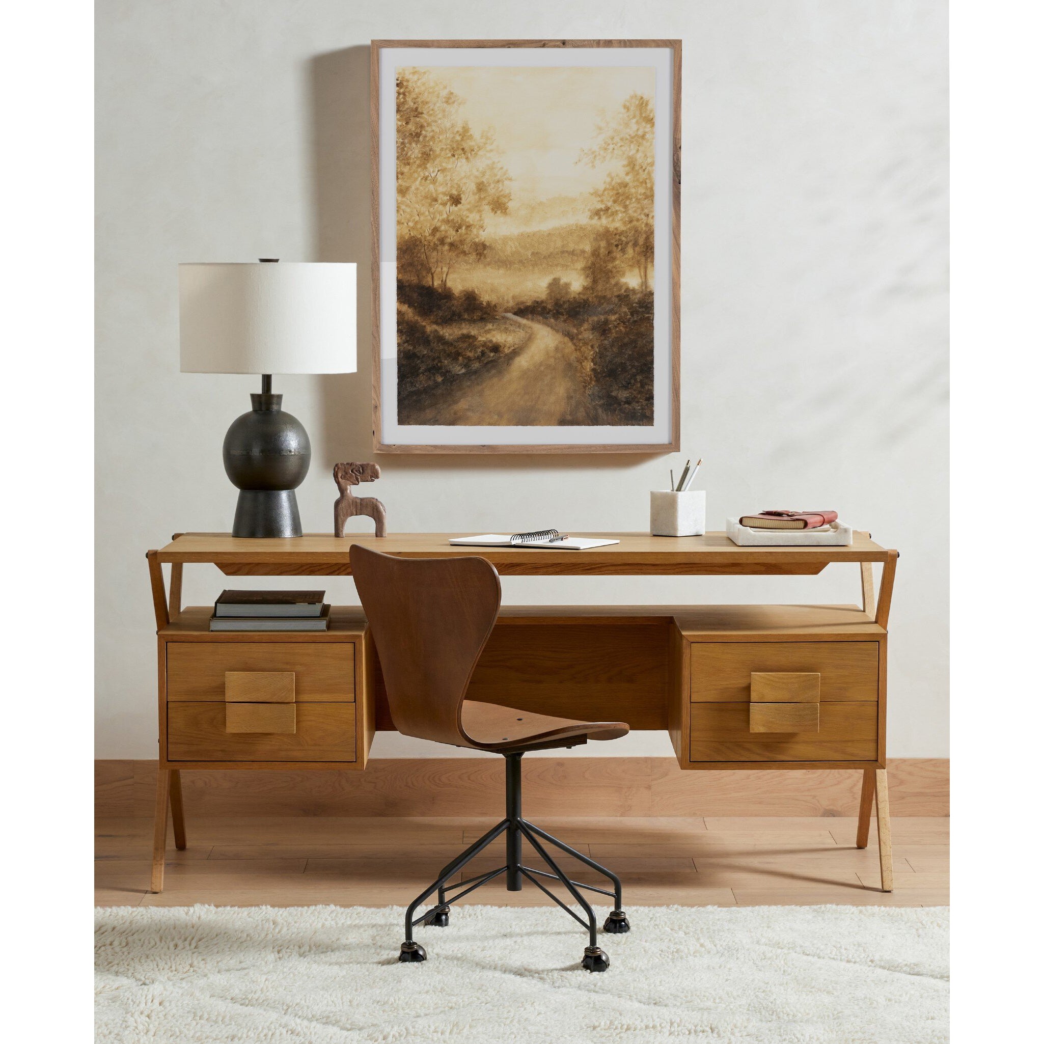 Wooden desk with chair, lamp, and framed artwork in a room setting.