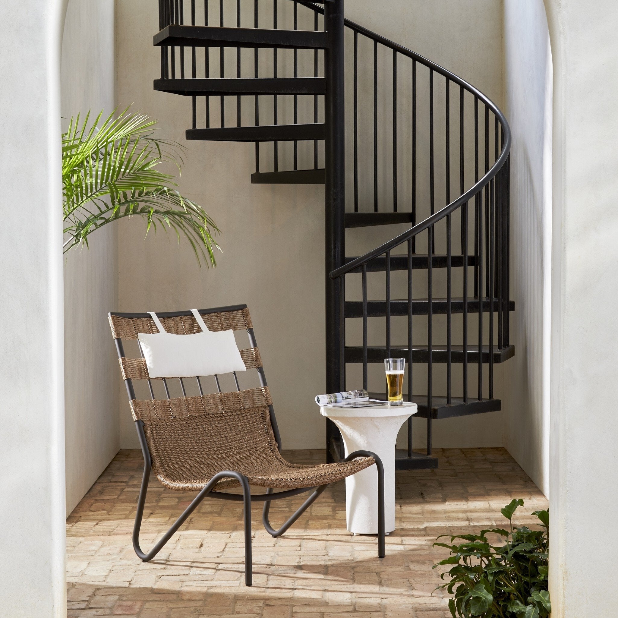 Chair with a plant and a glass of beer on a small patio area with a spiral staircase.