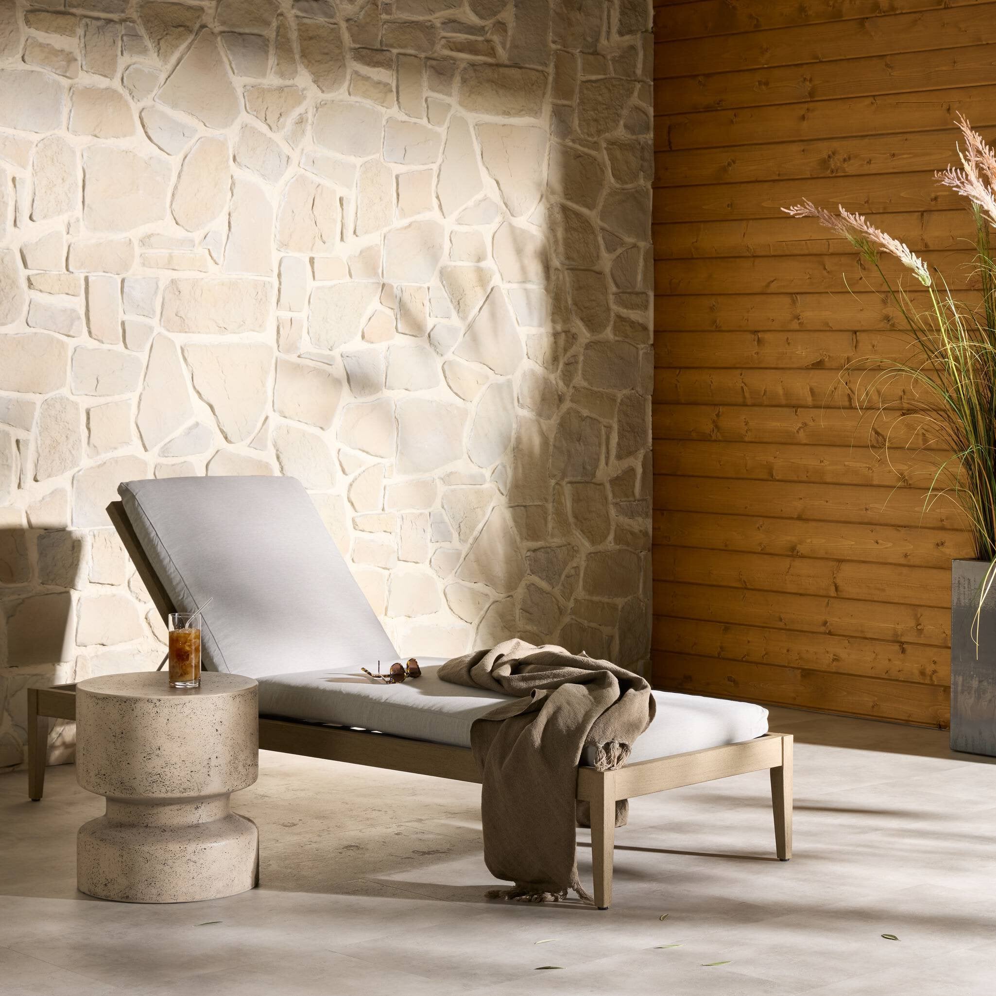 Modern lounge chair with a drink on a stone table against a stone wall.