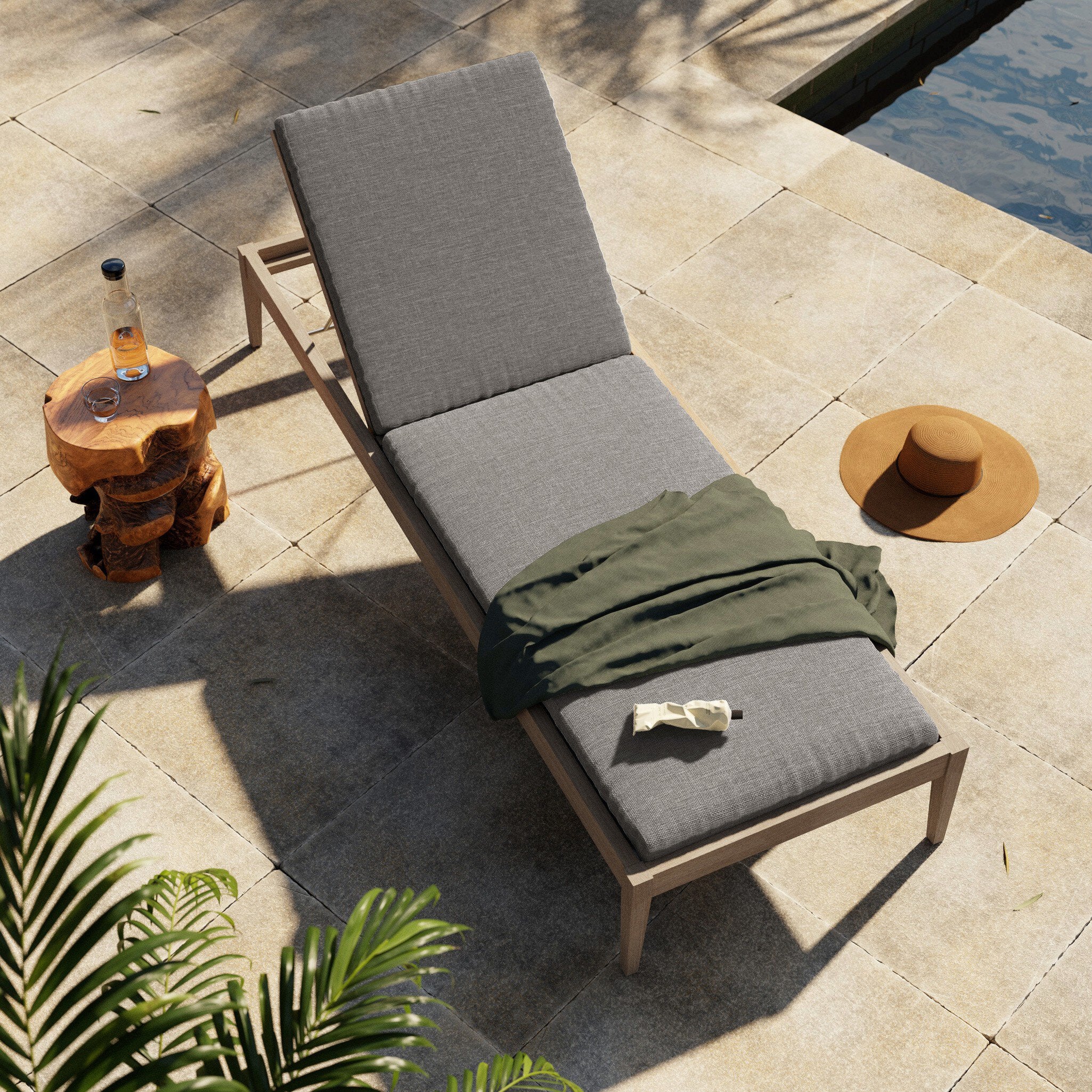 Gray lounge chair with a green towel on a stone patio by a pool