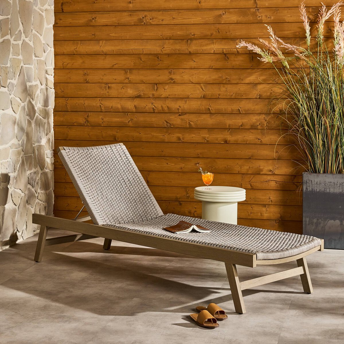 Wicker lounge chair with a drink on a small table against a wooden wall.