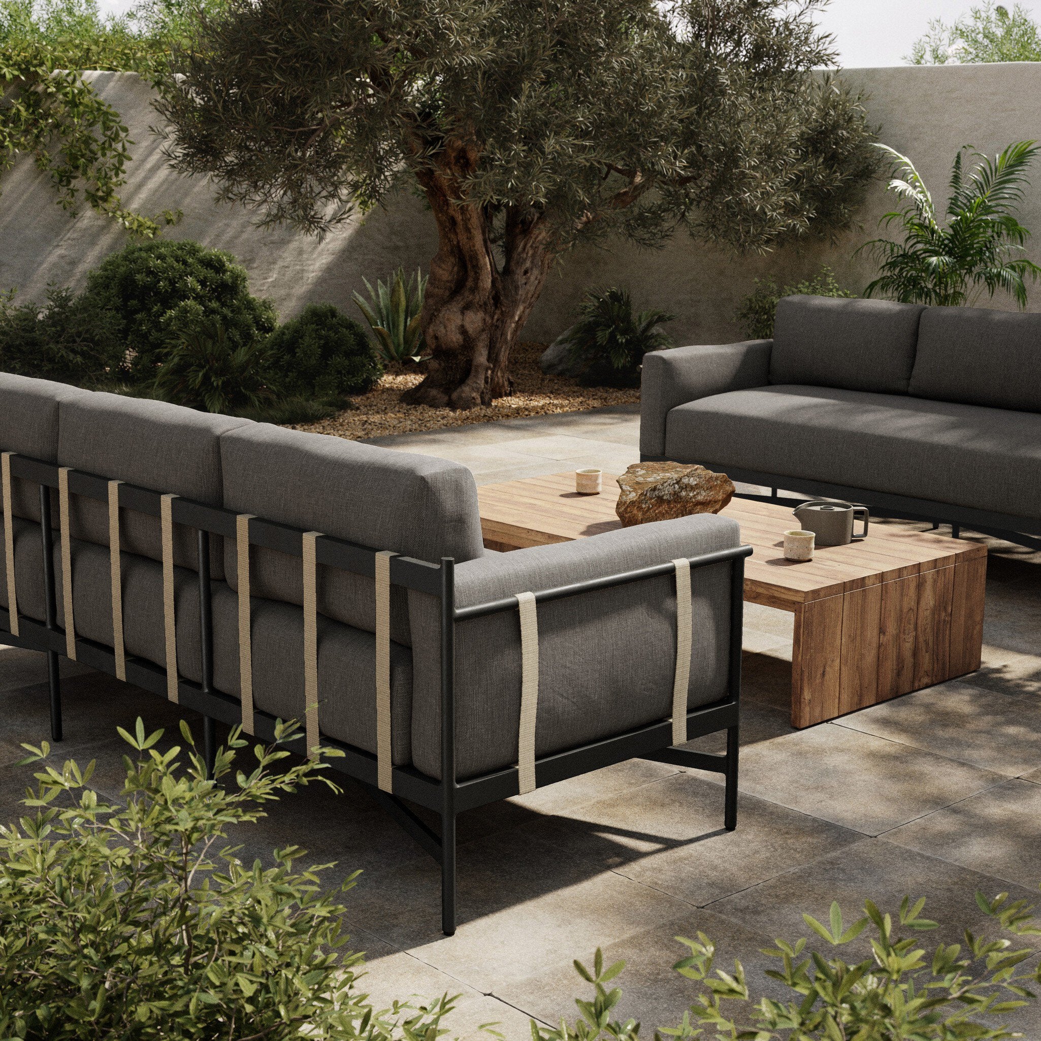 Outdoor patio furniture set with gray cushions and wooden coffee table in a garden setting.