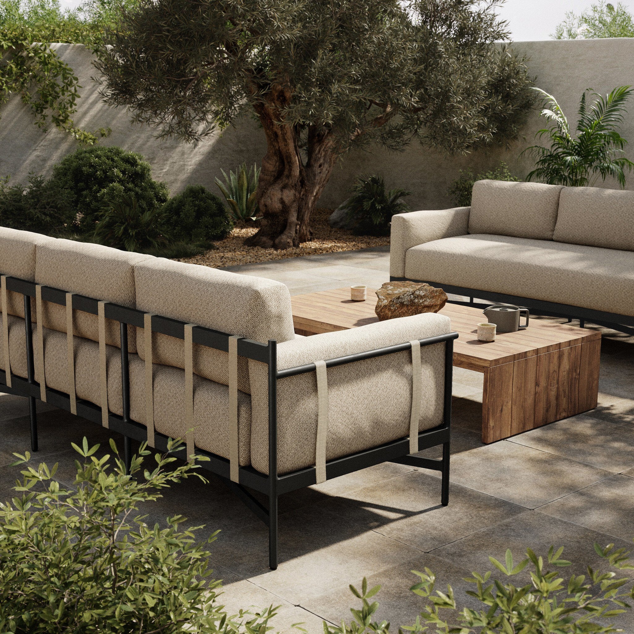 Outdoor patio setting with beige sofas and wooden coffee table in a garden.