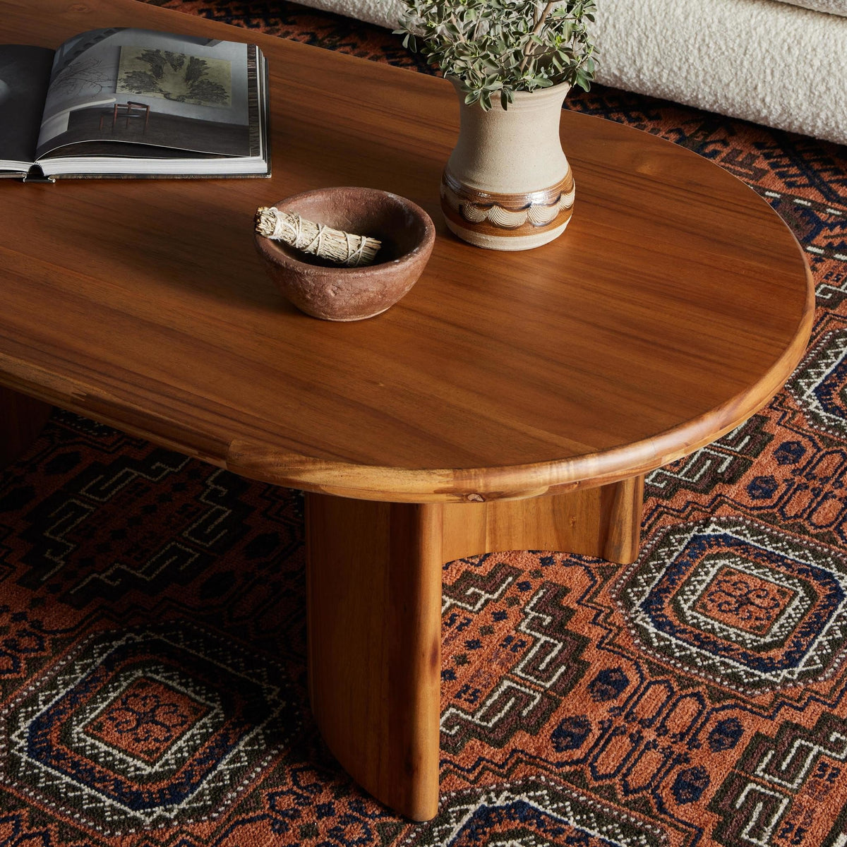 Wooden coffee table with a bowl, book, and vase on a patterned rug