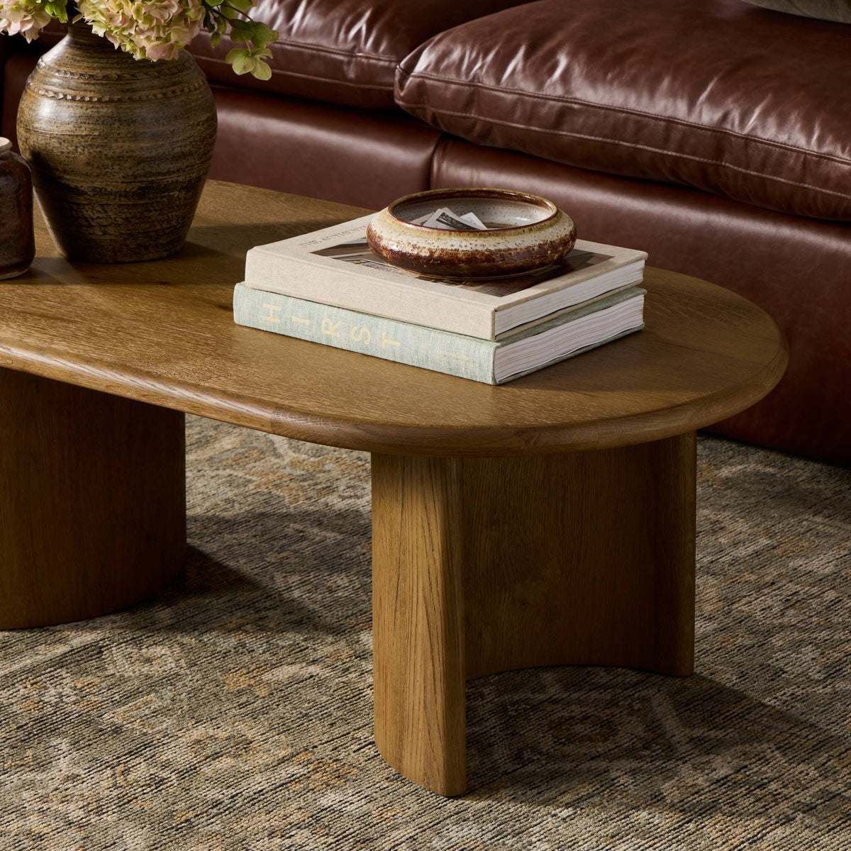 Wooden coffee table with books and a vase in front of a brown leather sofa.