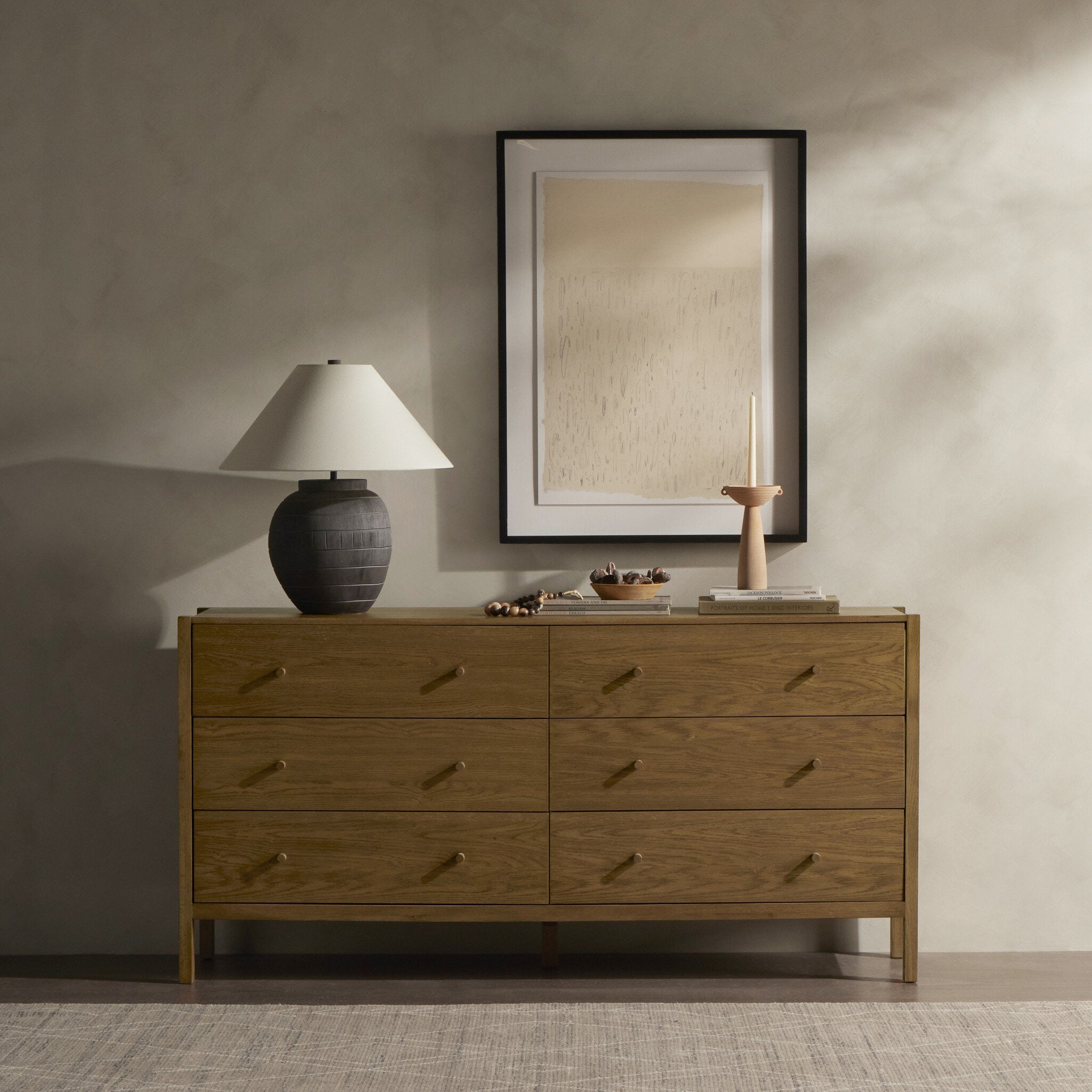 Wooden dresser with a lamp and decorative items against a neutral wall.