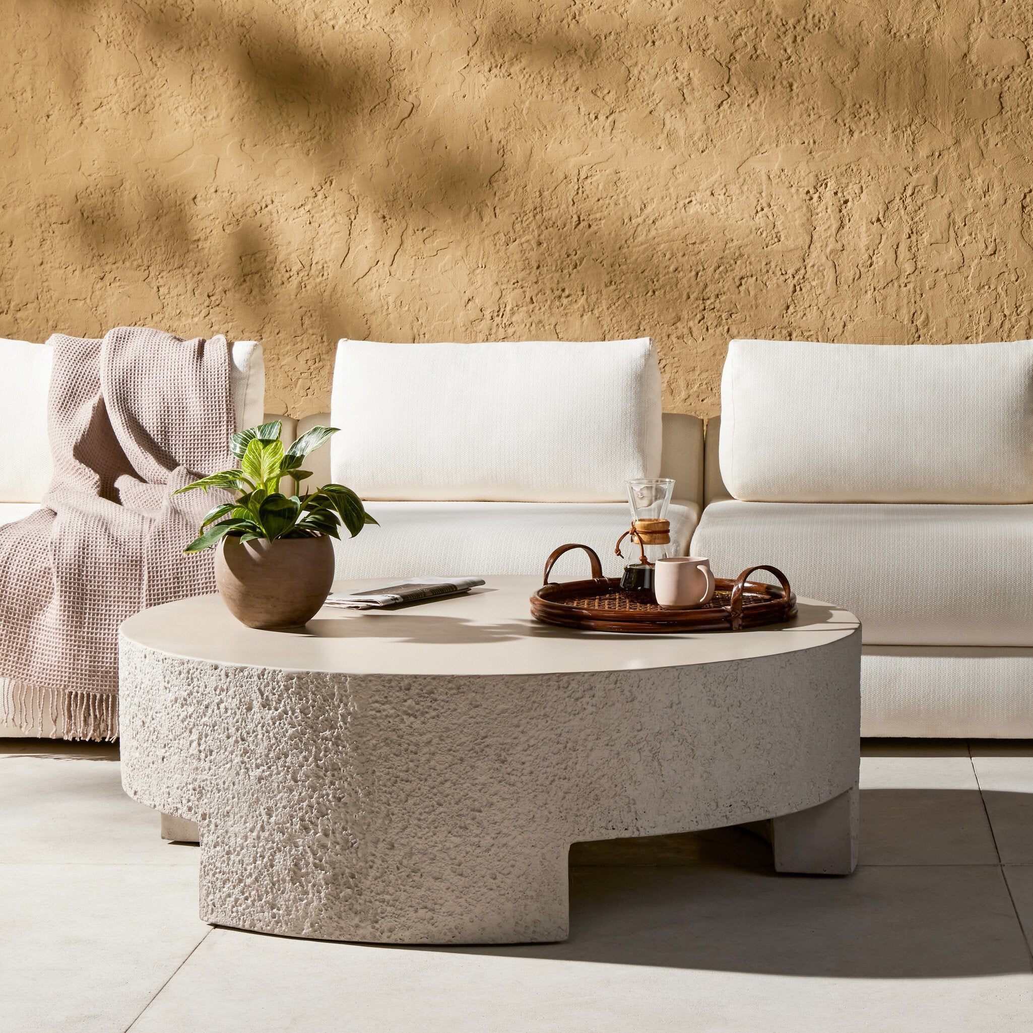 Round textured coffee table with decorative items in front of a white sofa against a beige wall.