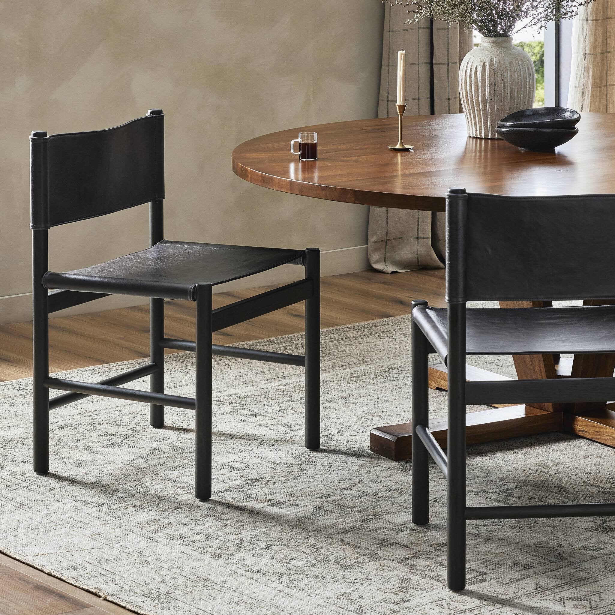 Two black dining chairs at a wooden dining table in a room with a textured wall and rug.