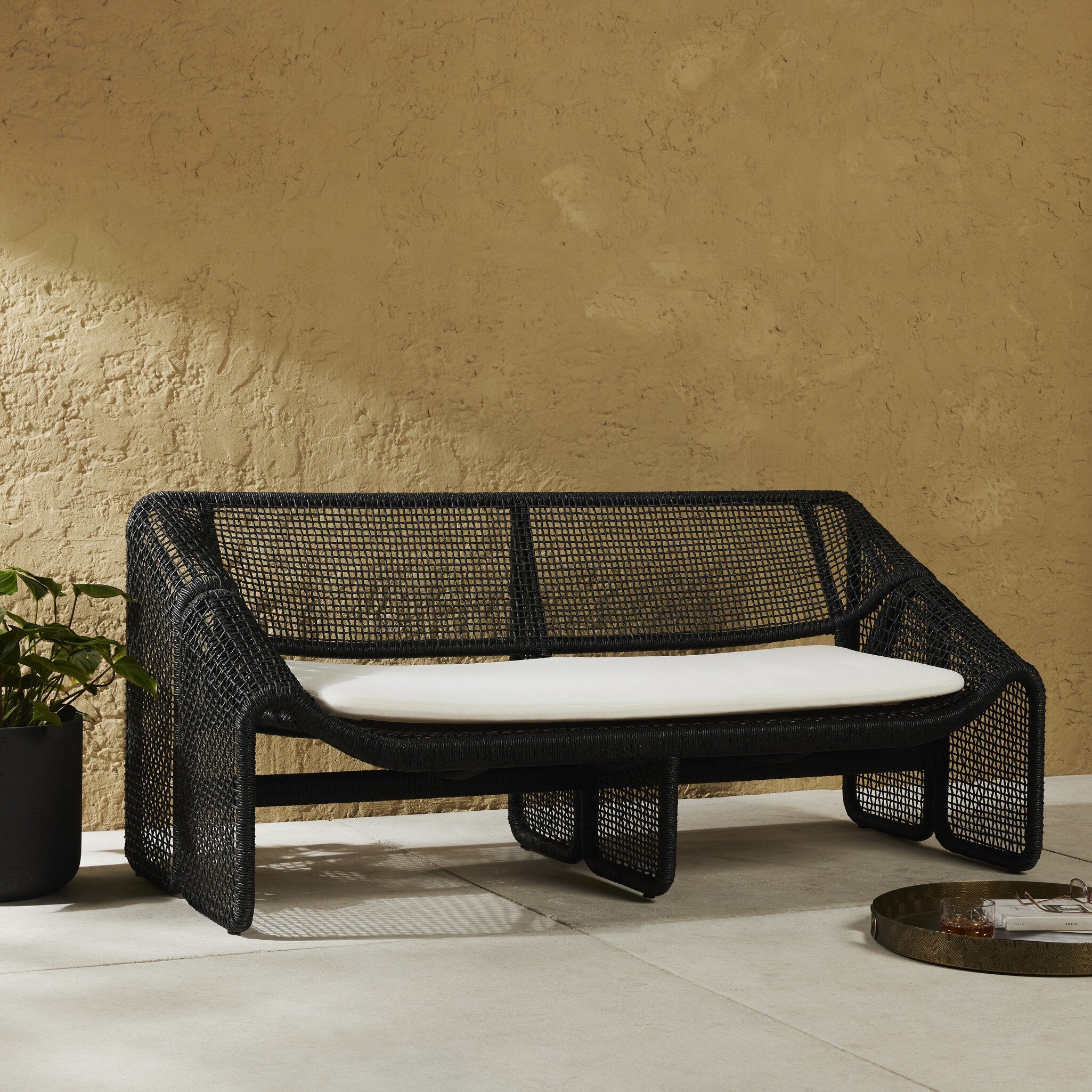 Black wicker outdoor sofa with white cushion against a beige wall.