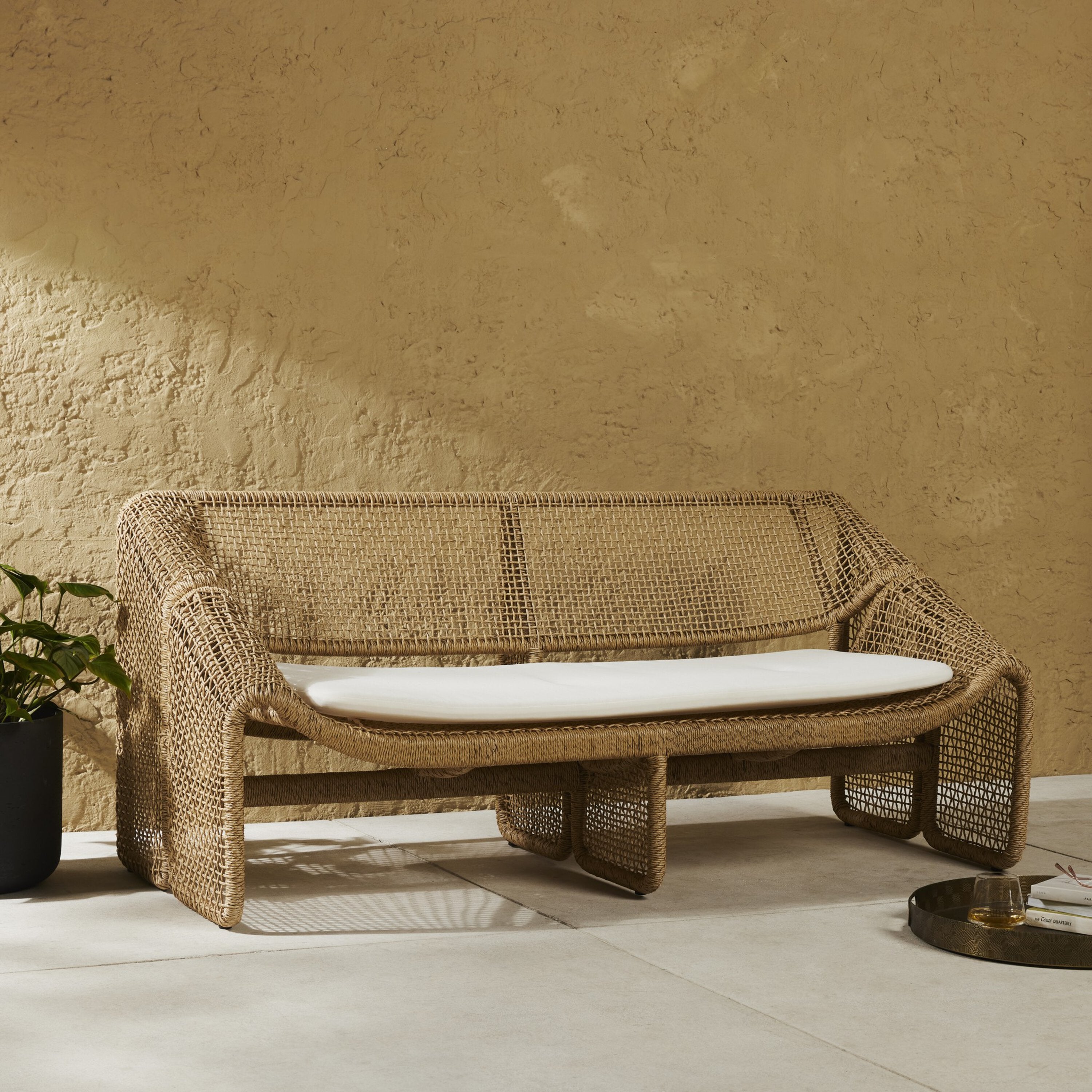 An outdoor sofa with a beige all-weather wicker frame and a white cushion.