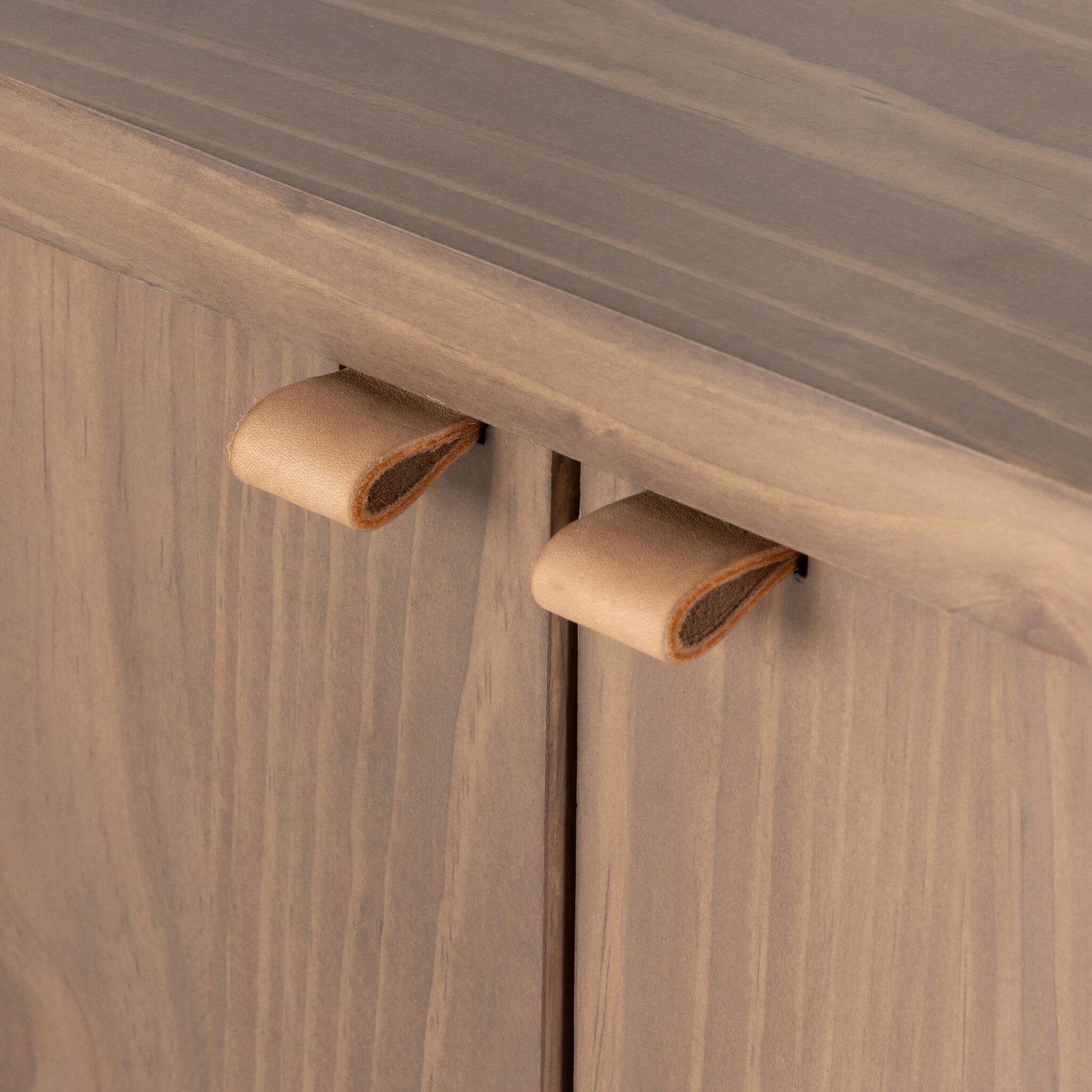 Wooden cabinet with round, brown leather handles on a wooden surface.