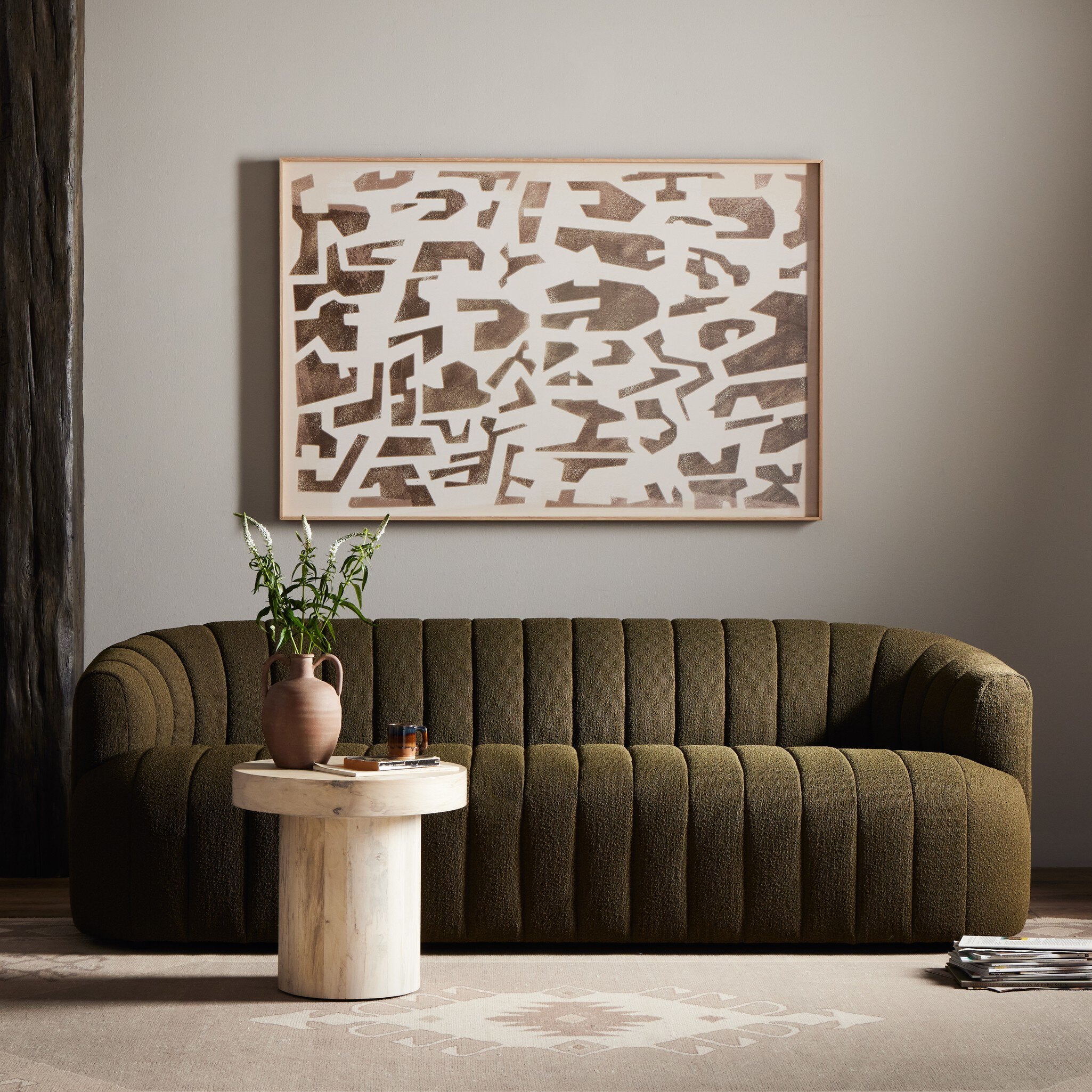 Green sofa in a living room with abstract art and a wooden side table.