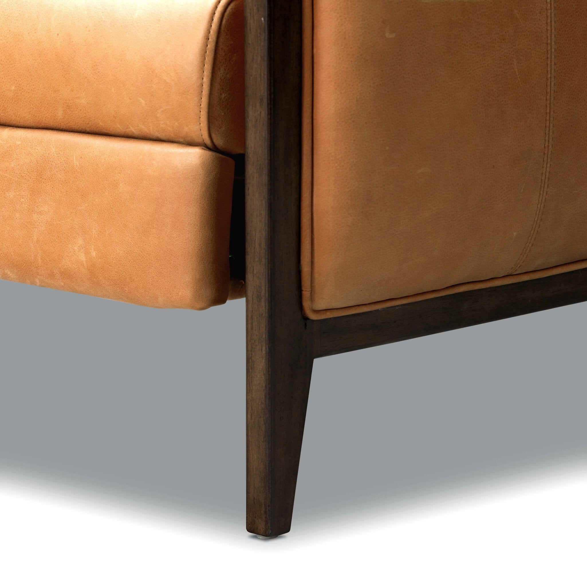 Close-up of a brown leather chair corner with wooden legs on a gray background