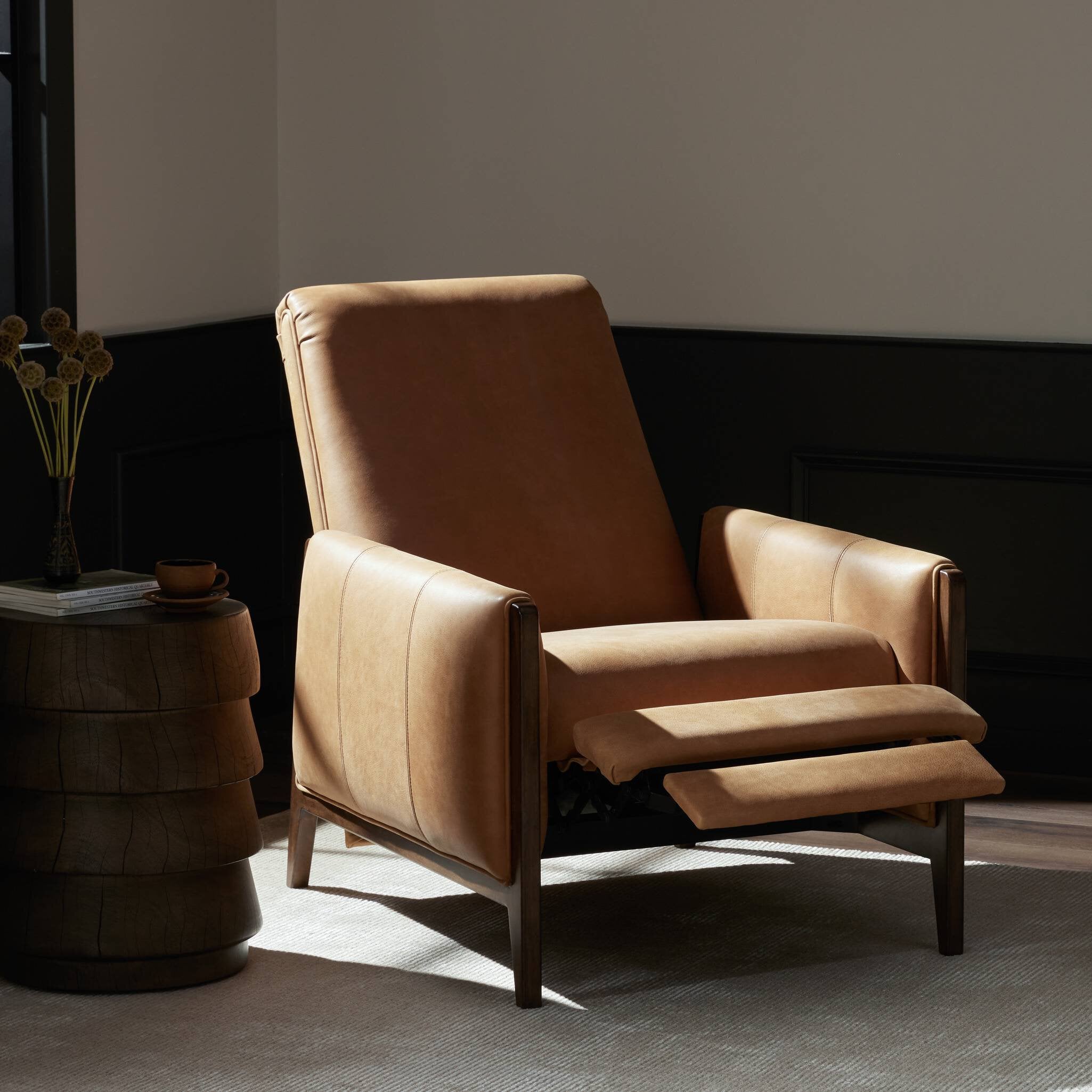 Brown leather armchair with ottoman in a room with a dark wall and light floor.
