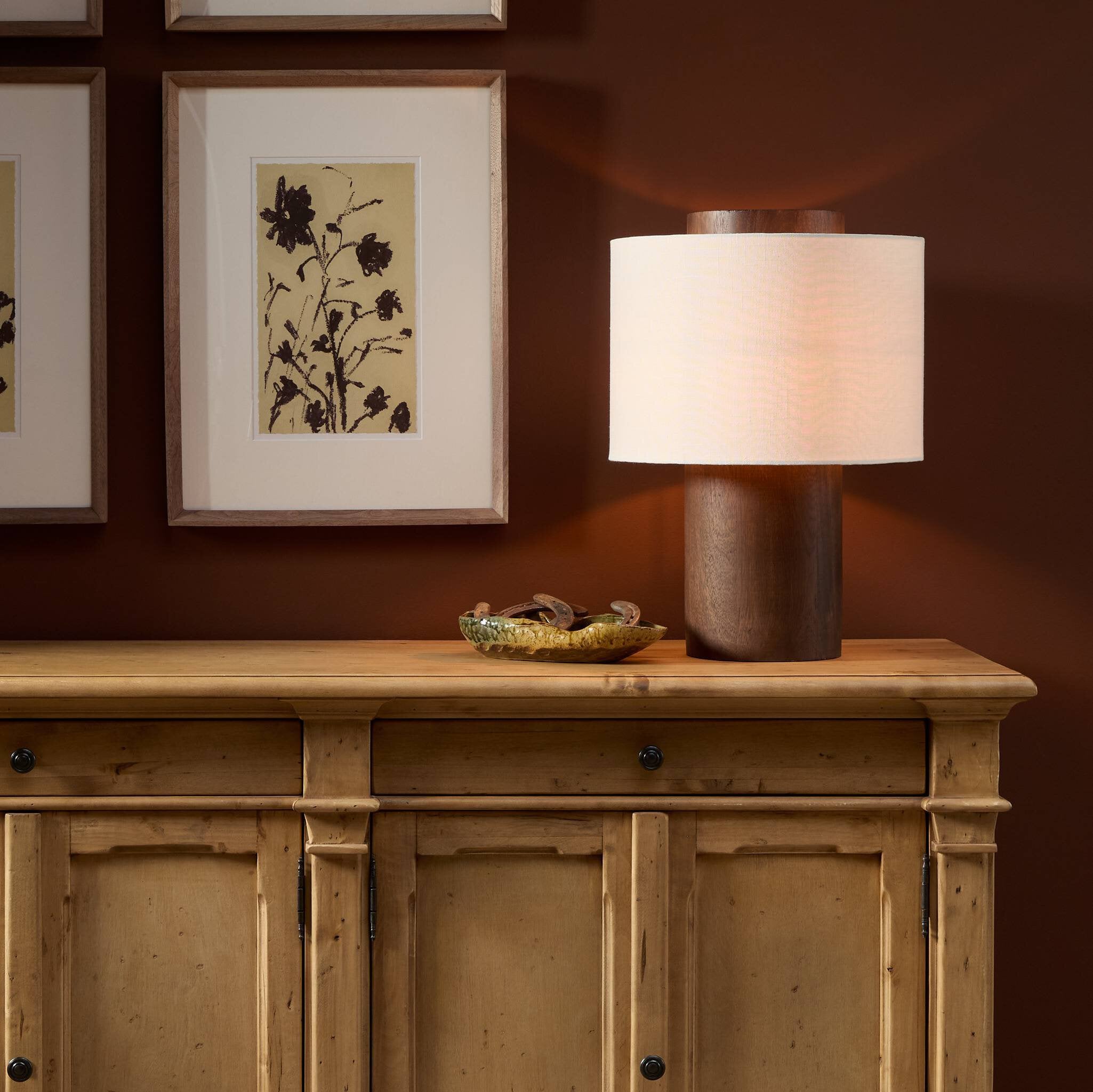 Lamp on a wooden cabinet with framed artwork in the background