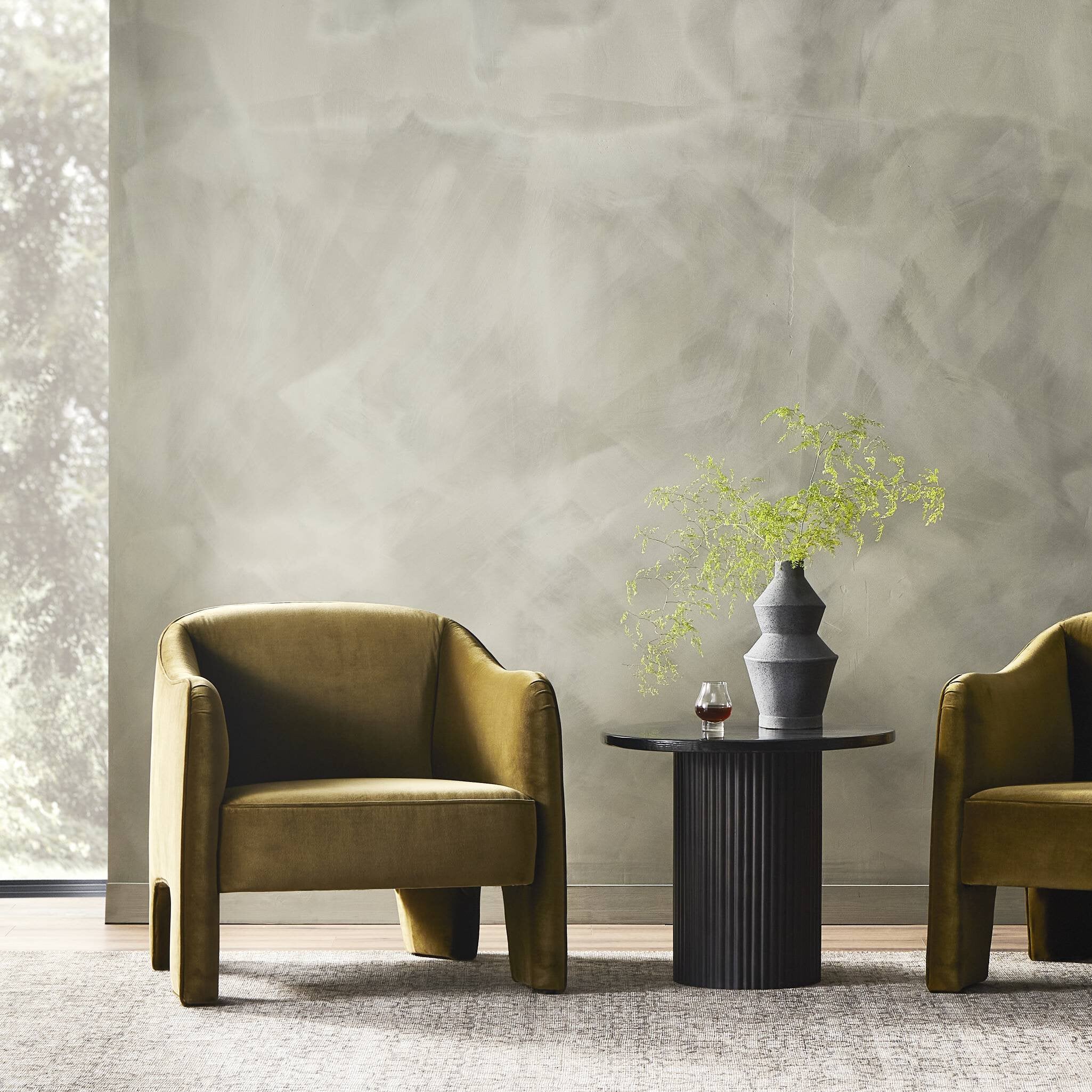 Two mustard yellow armchairs with a small round table and vase against a textured gray wall.