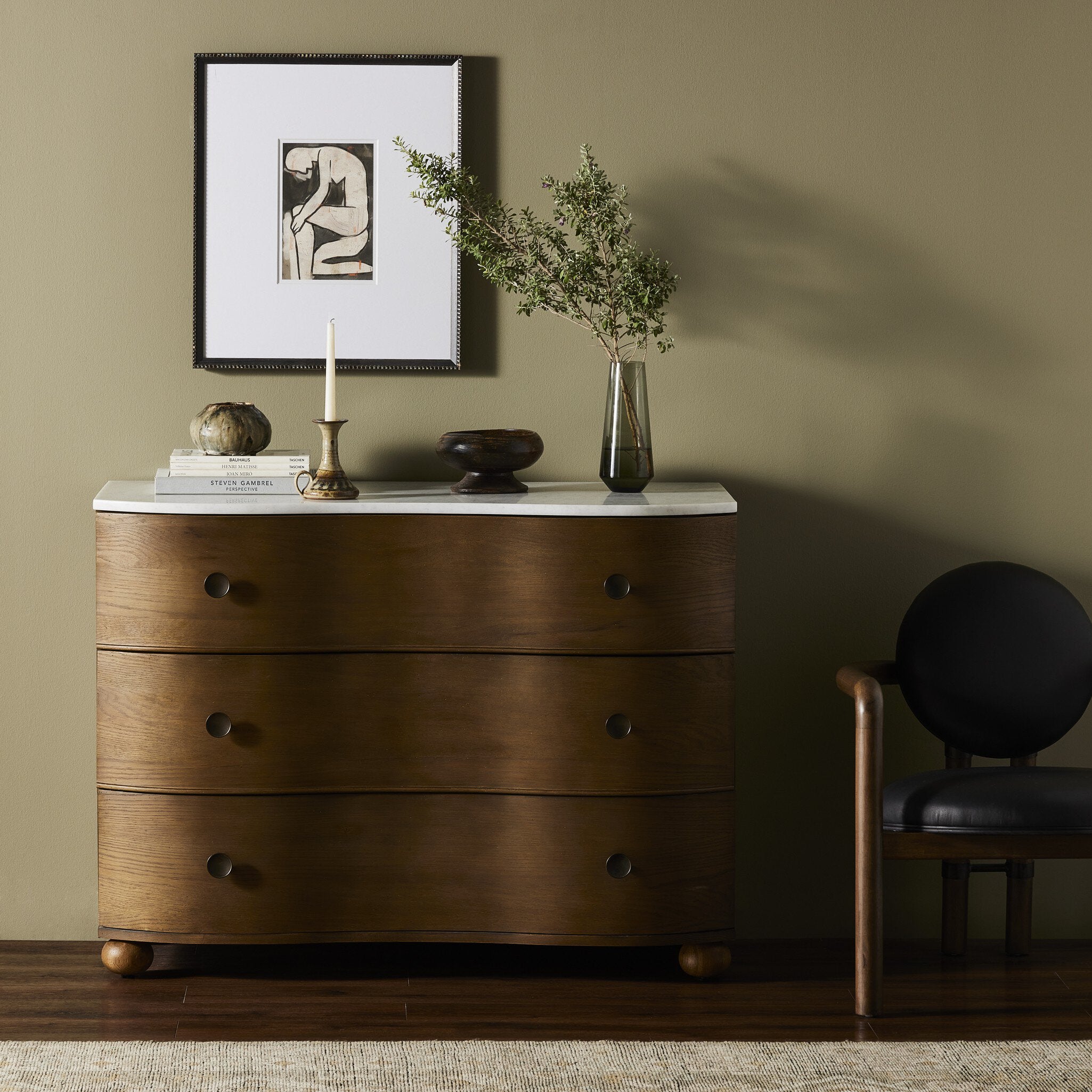 Wooden dresser with marble top against a beige wall with a framed picture and plant.