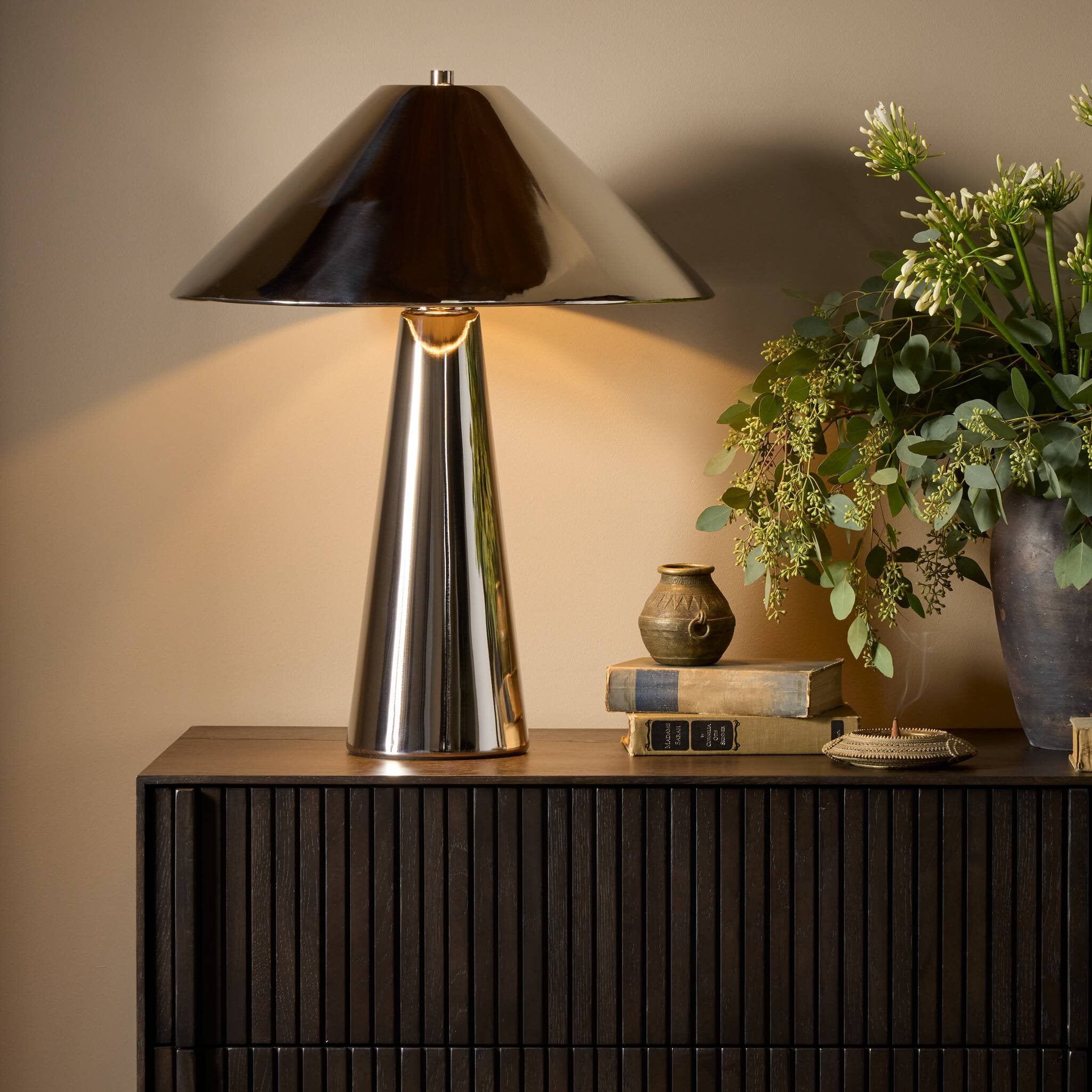 Modern table lamp with a black shade on a wooden surface with books and a plant.