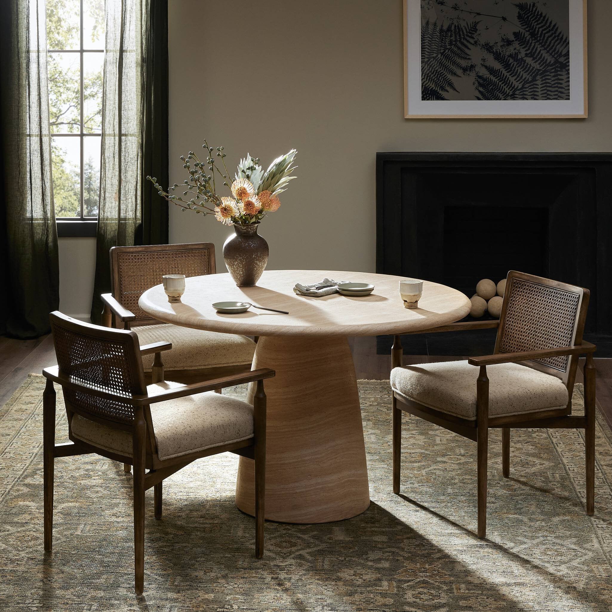Dining room with a round concrete table and chairs, vase with flowers, and fireplace.