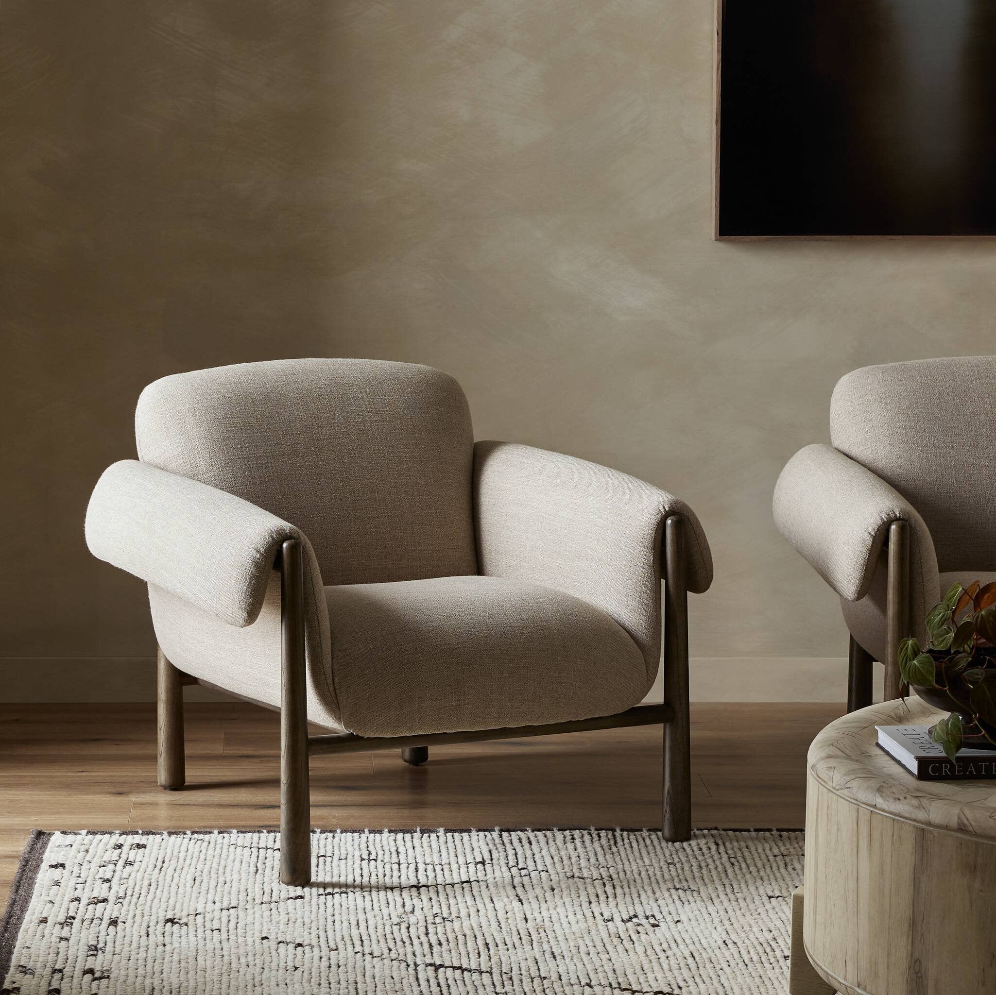 Two beige armchairs in a room with a textured wall and wooden floor.