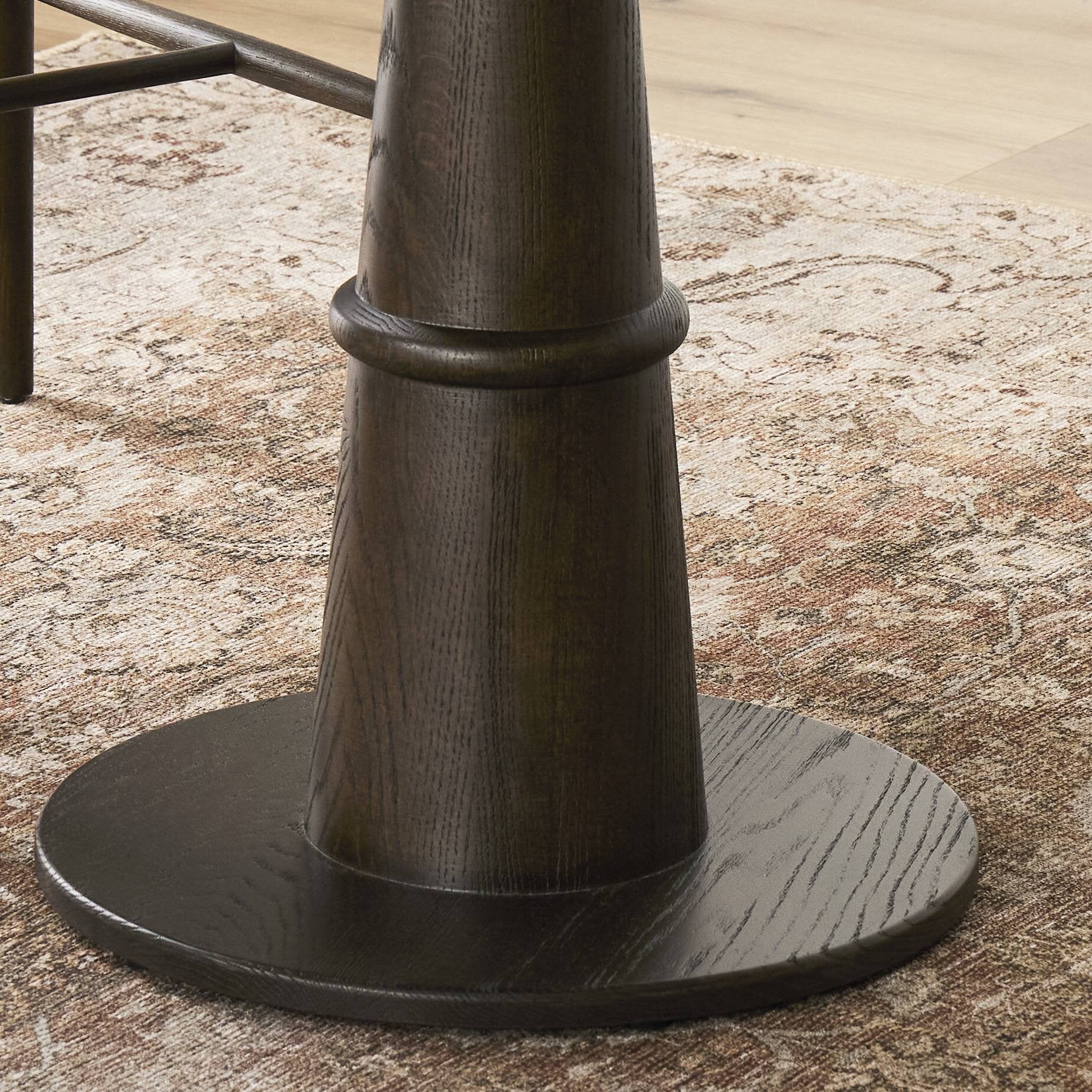 Dark wooden pedestal dining table base on a textured rug