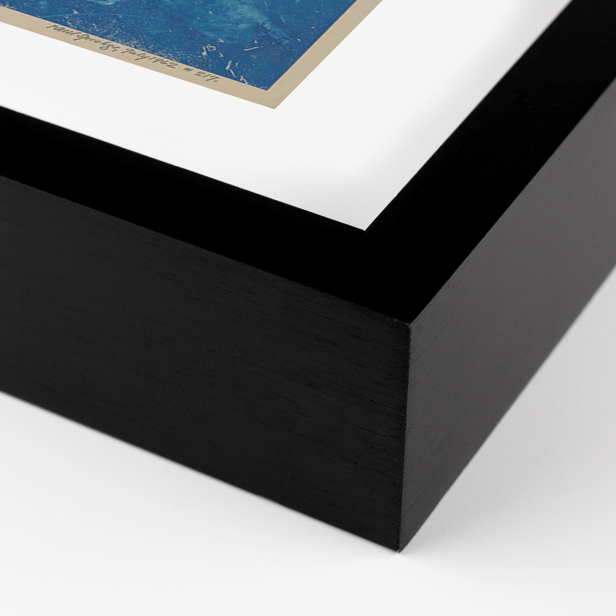 Close-up of a black framed artwork with a white mat and blue print inside.