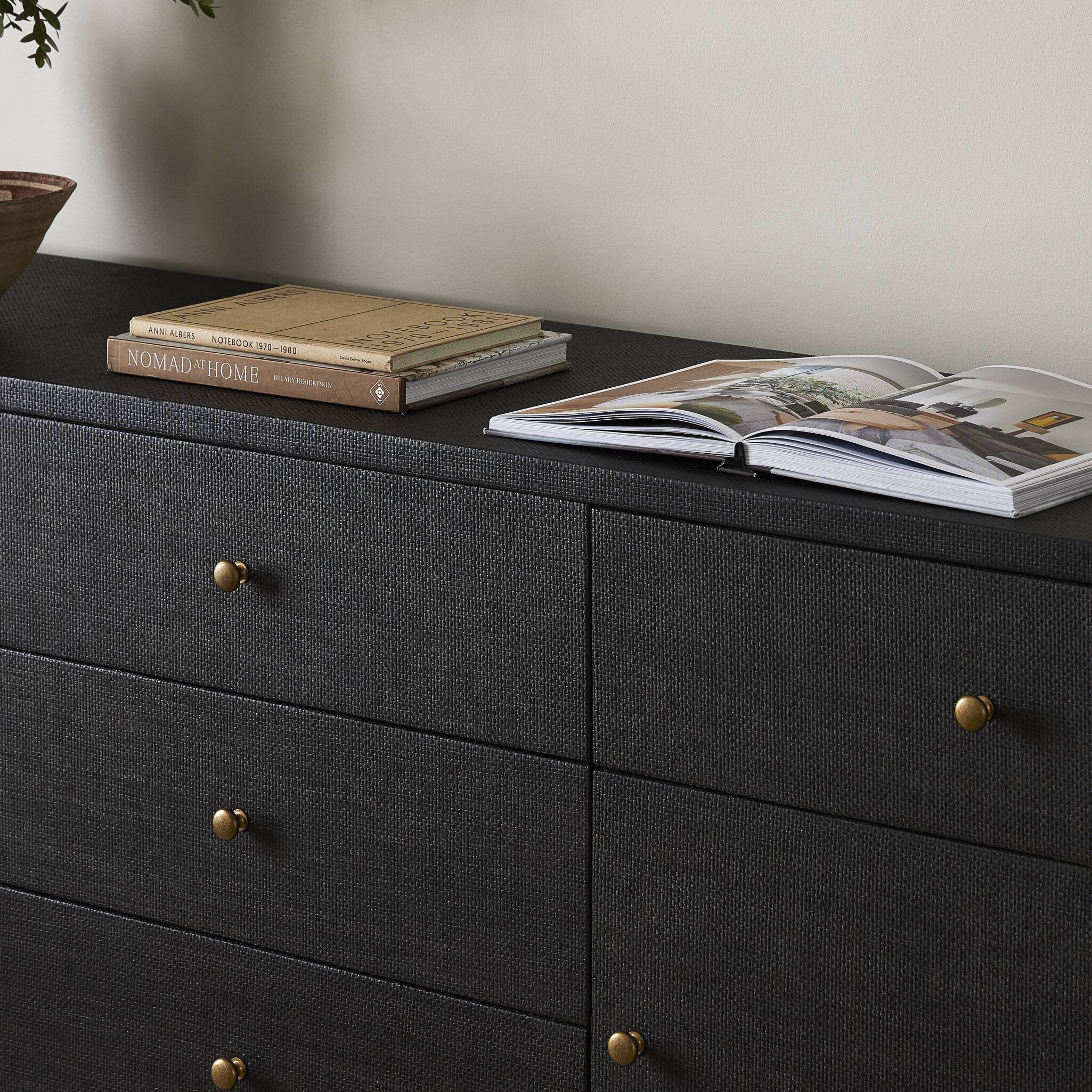 Black dresser with gold knobs featuring books and a magazine on top.