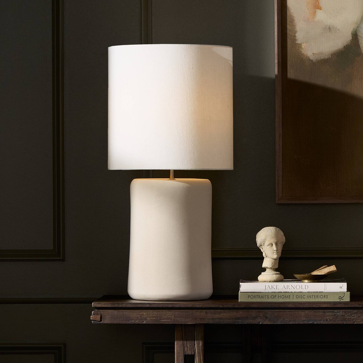 Table lamp with a white ceramic base and beige shade on a dark surface.