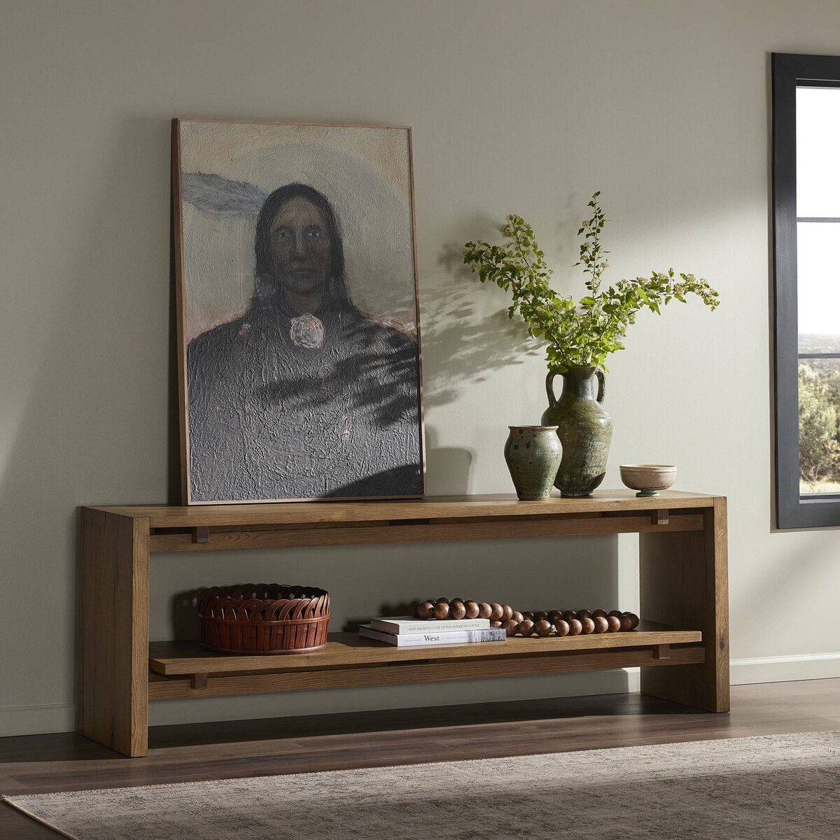 Wooden console table with decorative items in a room with a portrait and window.