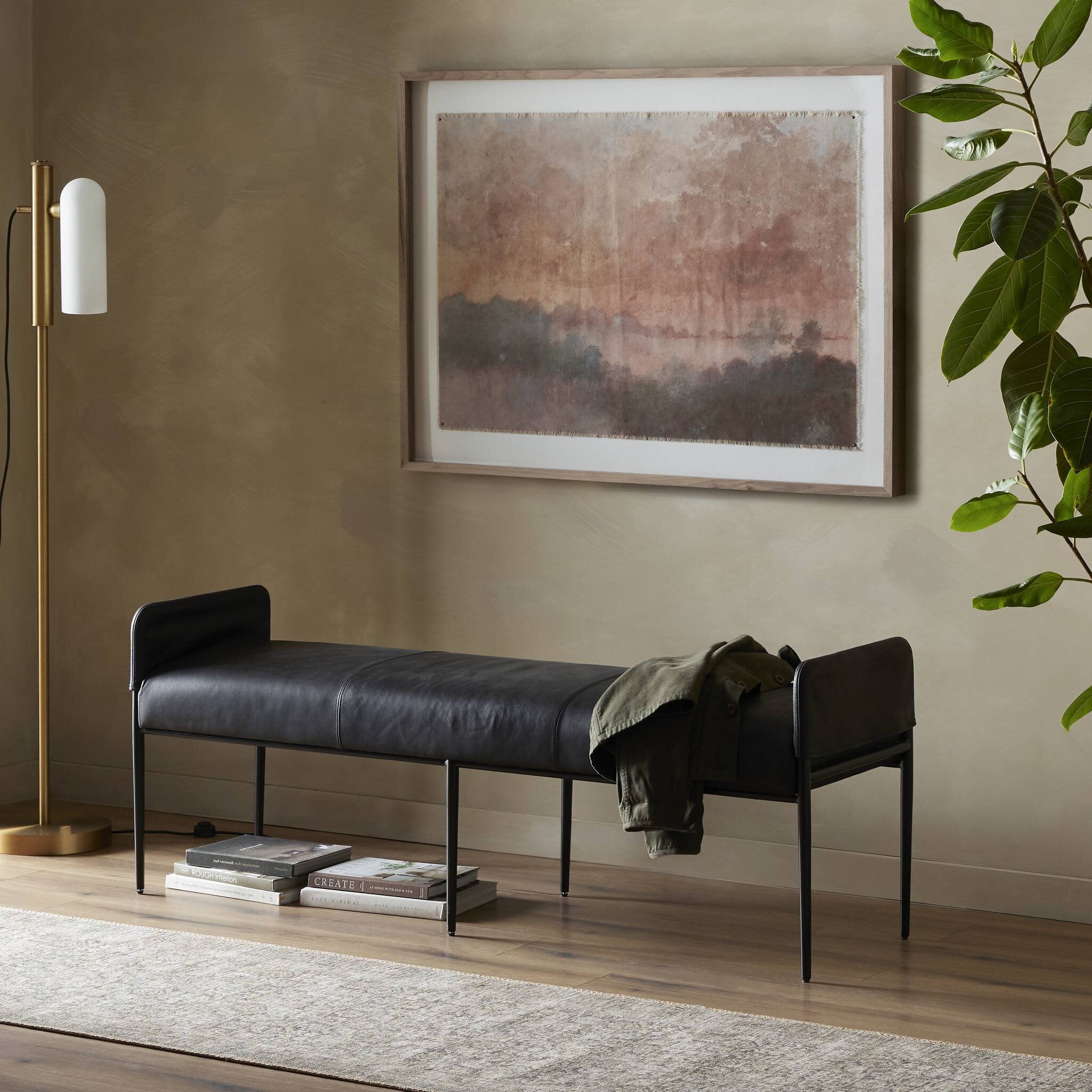 Modern black leather bench in a room with a painting, lamp, and plant.