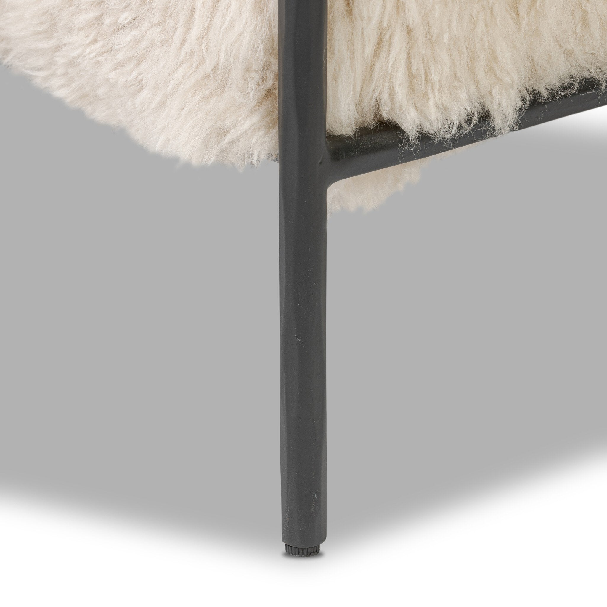 Close-up of a chair with a fluffy white cushion and a dark metal leg on a light gray background