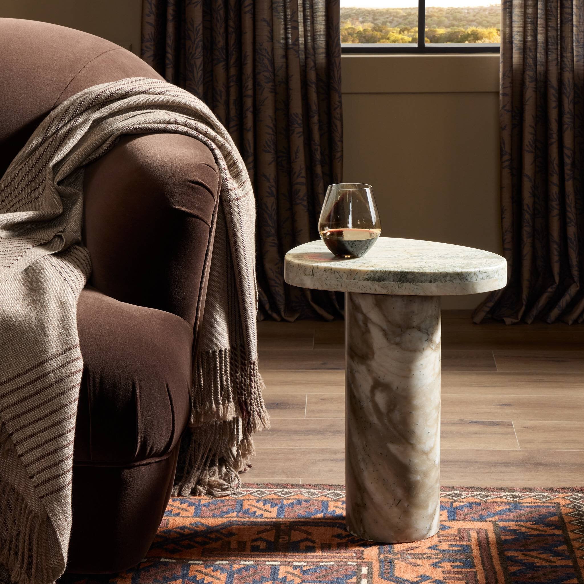 Stone side table with a glass of wine next to a brown armchair draped with a blanket.