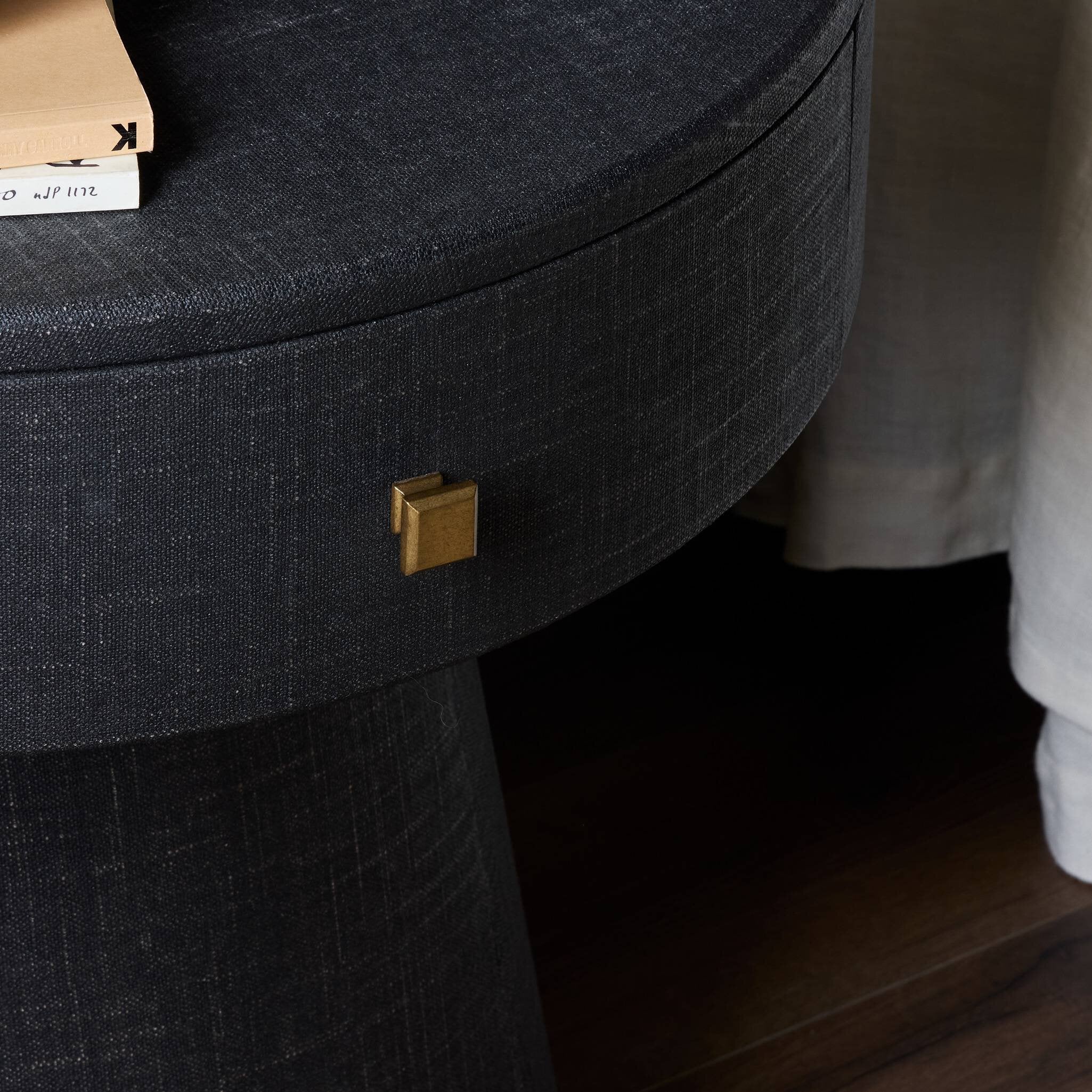 Close-up of a black fabric nighstand drawer with a gold handle on a wooden floor.