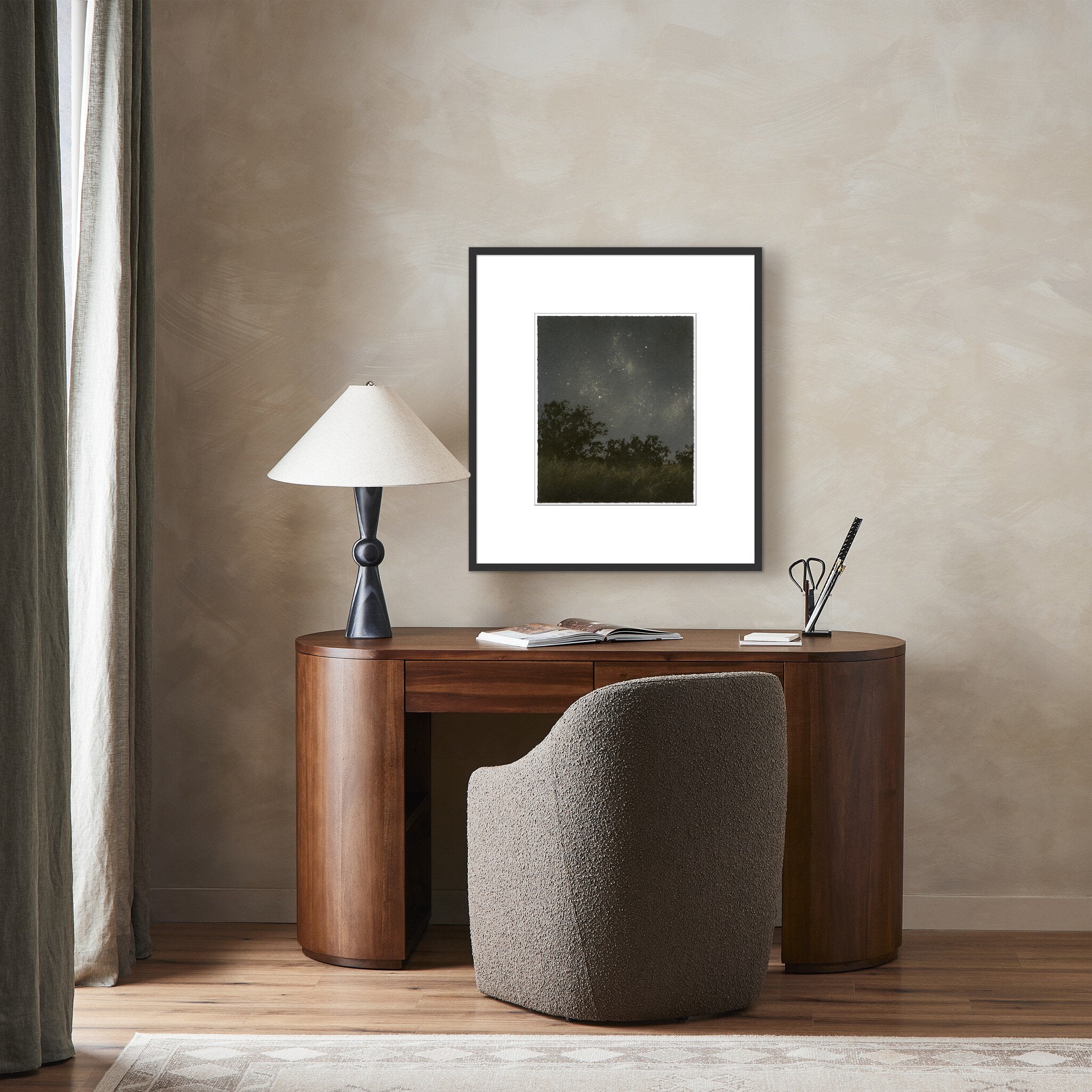 Wooden desk with a lamp, framed picture, and chair against a beige wall.