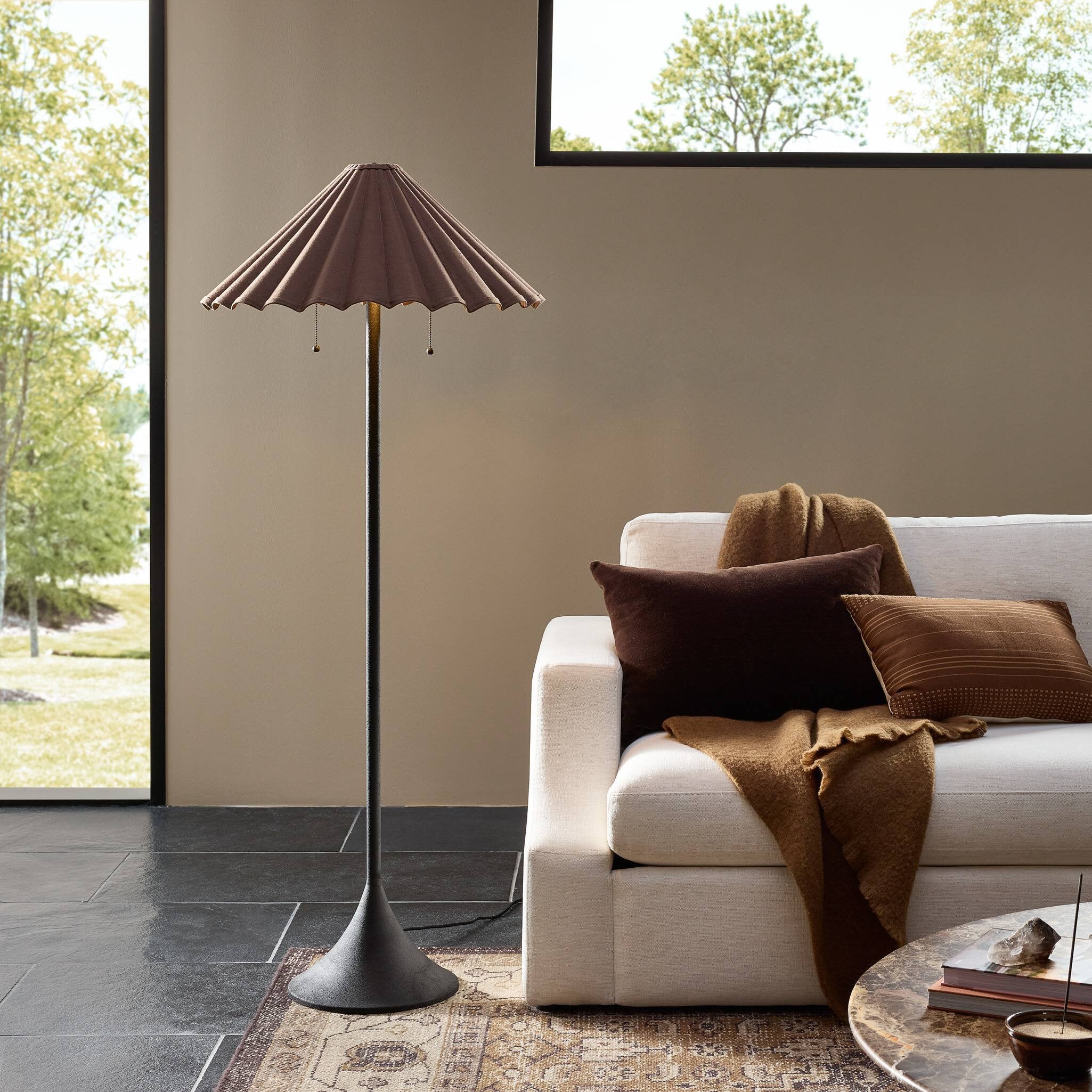 Floor lamp next to a white sofa with brown cushions and a blanket in a living room.